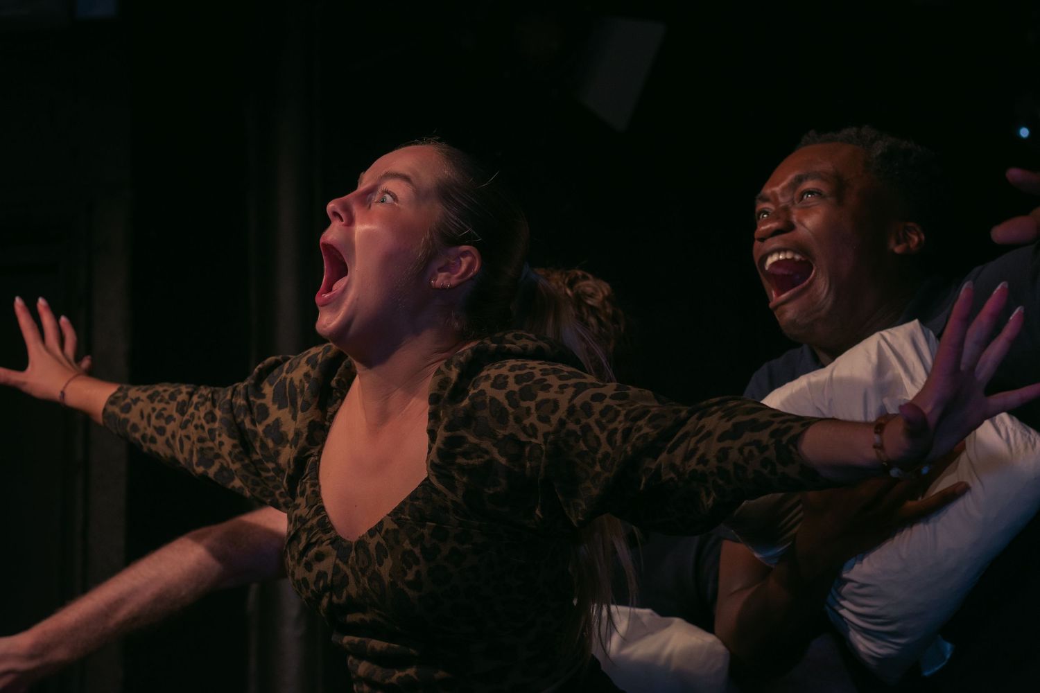 People showing dramatic reactions while seated in a dark theater-like setting.