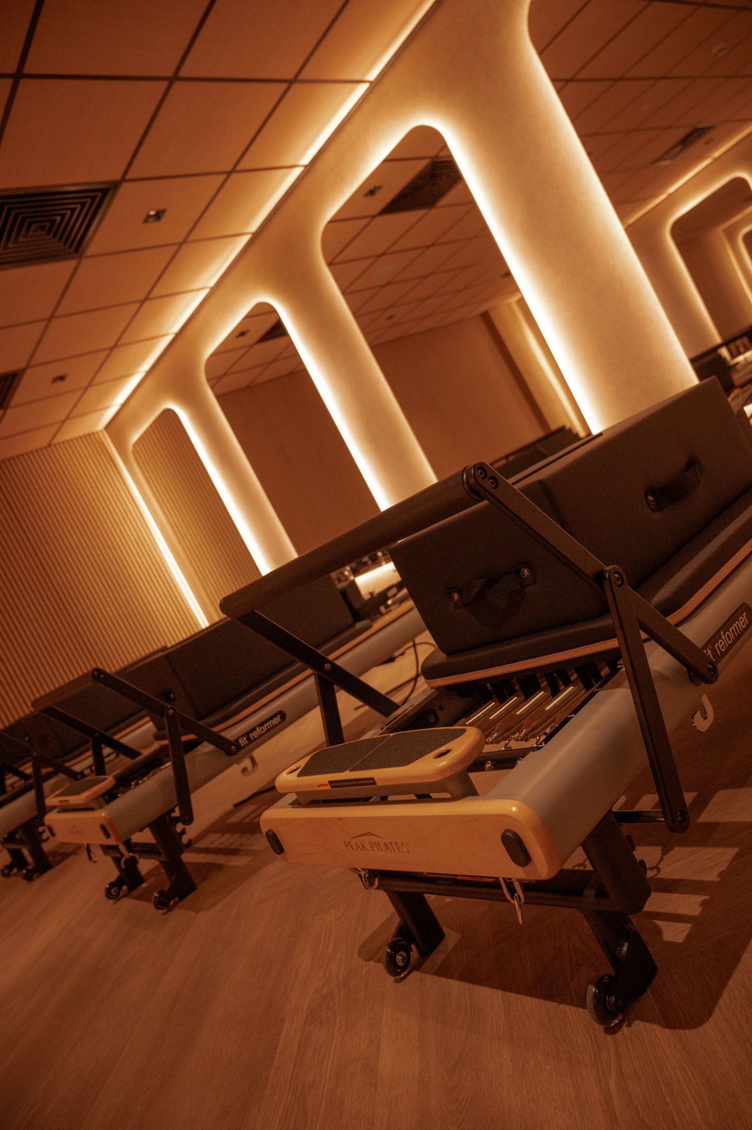 Luxury Pilates studio with reformer machines and warm amber arch lighting on textured walls.