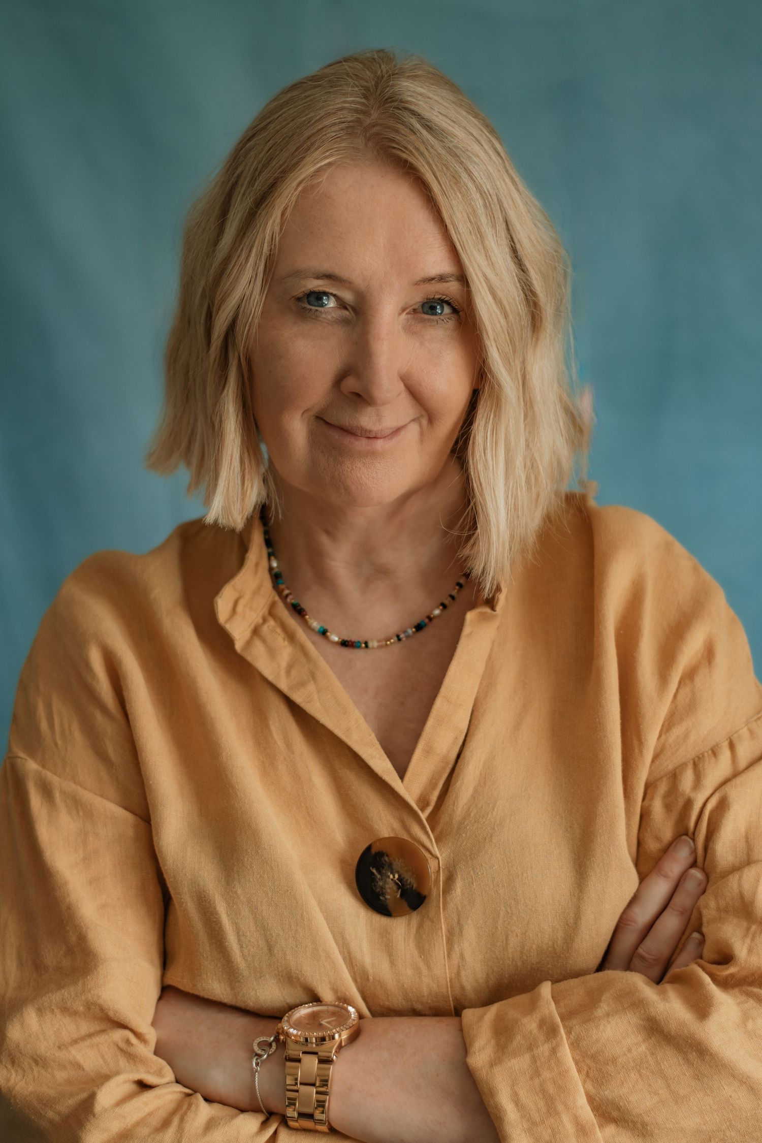 Professional portrait in warm yellow blouse with statement button against teal background.