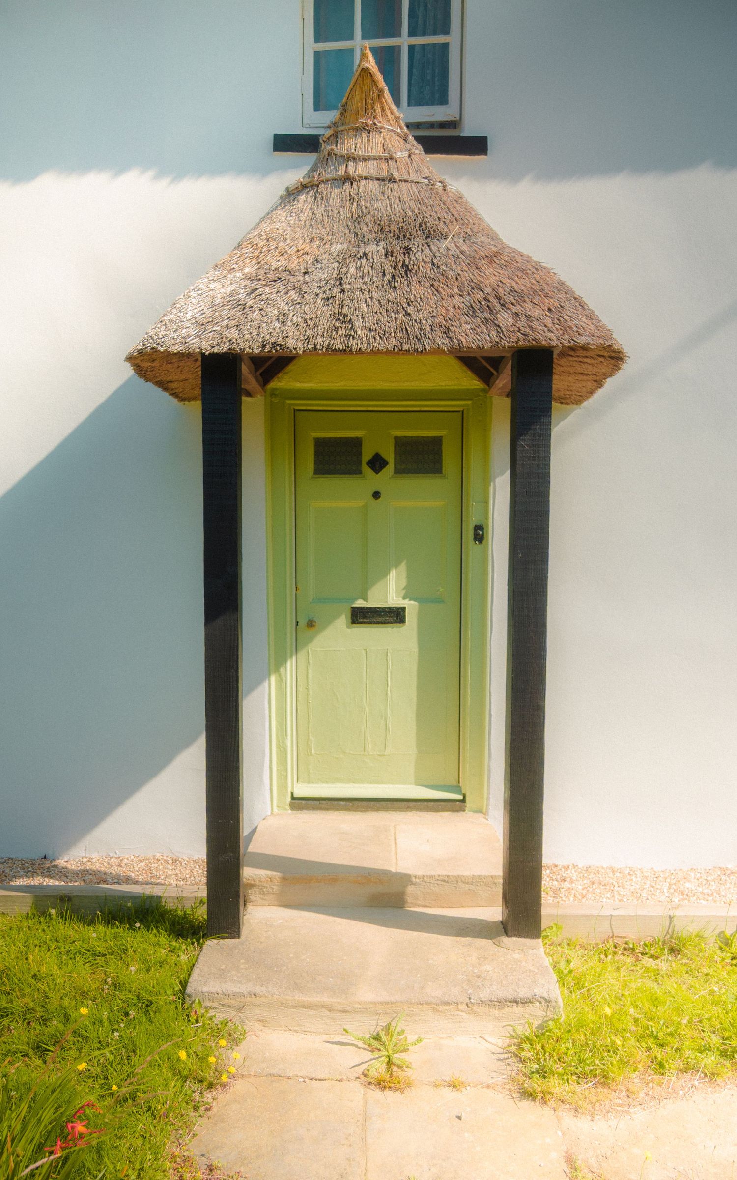 Lime green door with thatched roof overhang against white wall in natural sunlight.