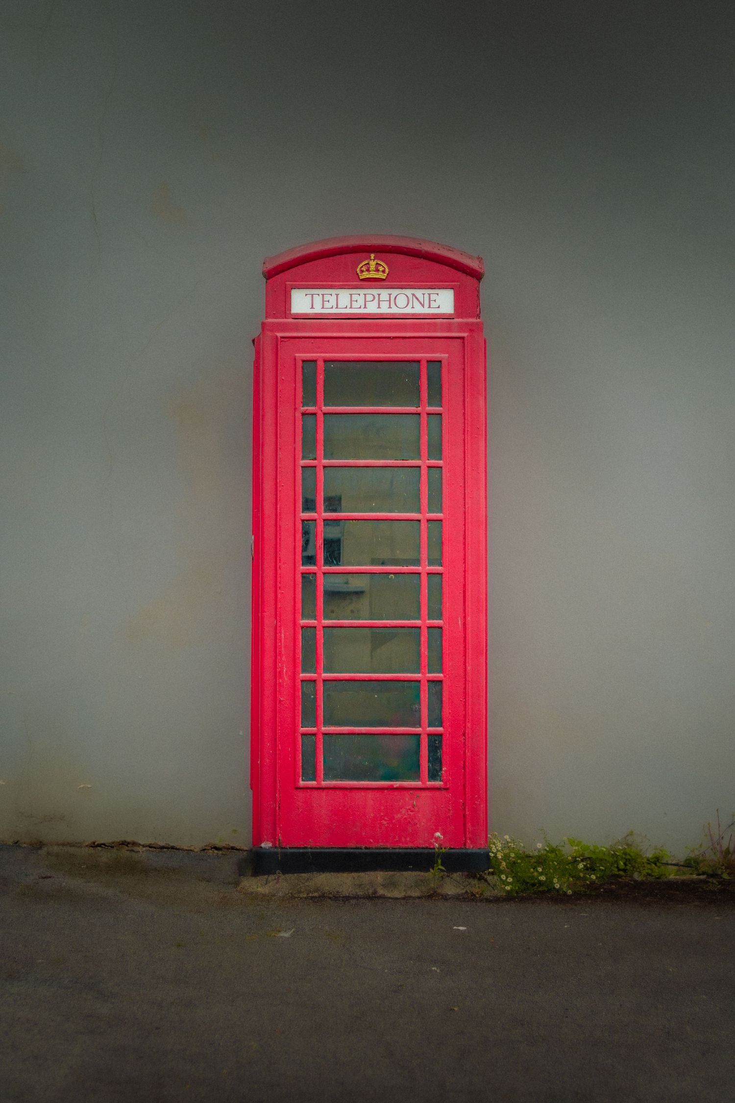 Classic red British telephone booth against a grey wall in moody lighting.