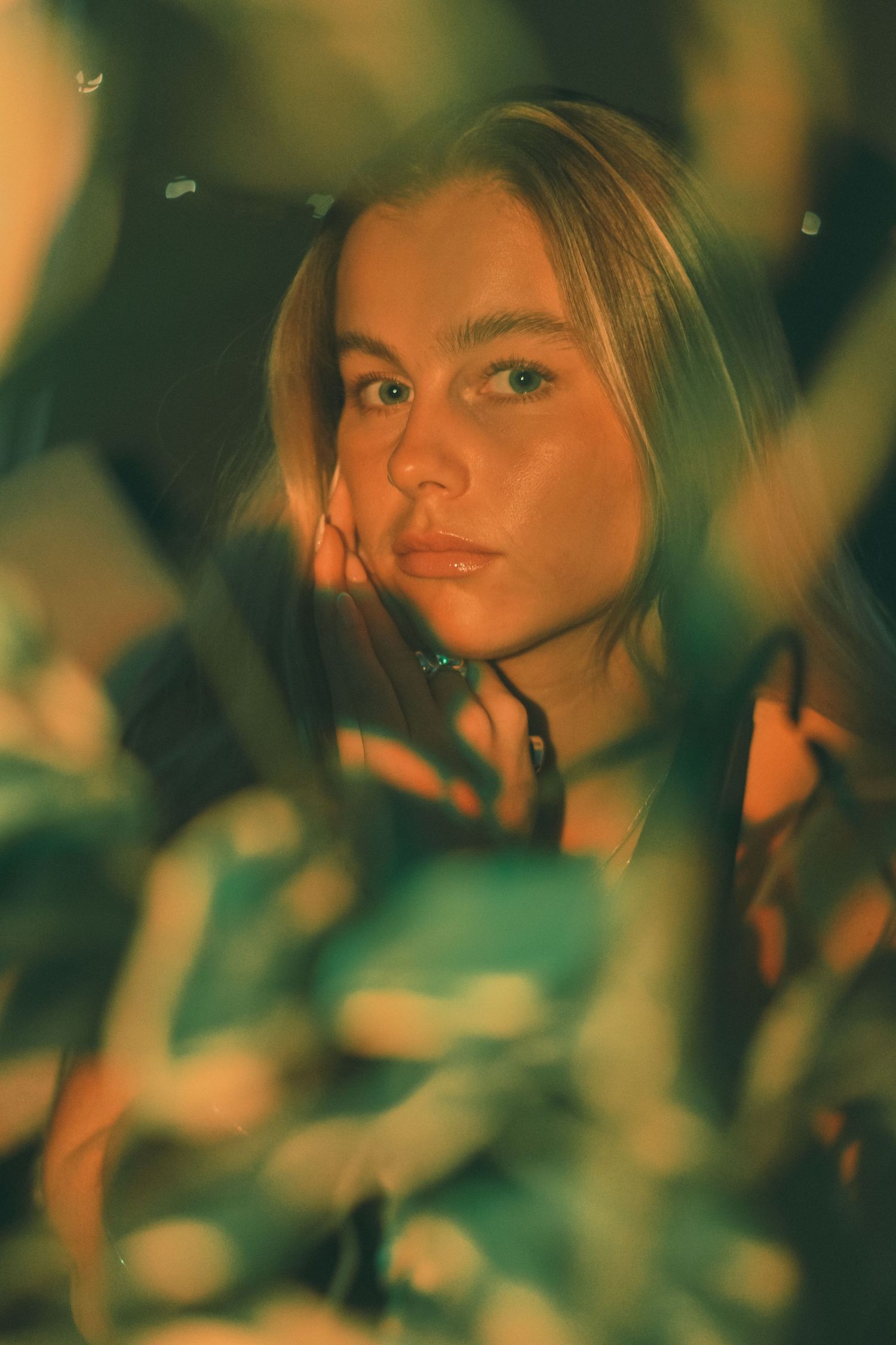 Portrait through foliage with warm tones and natural lighting effects.