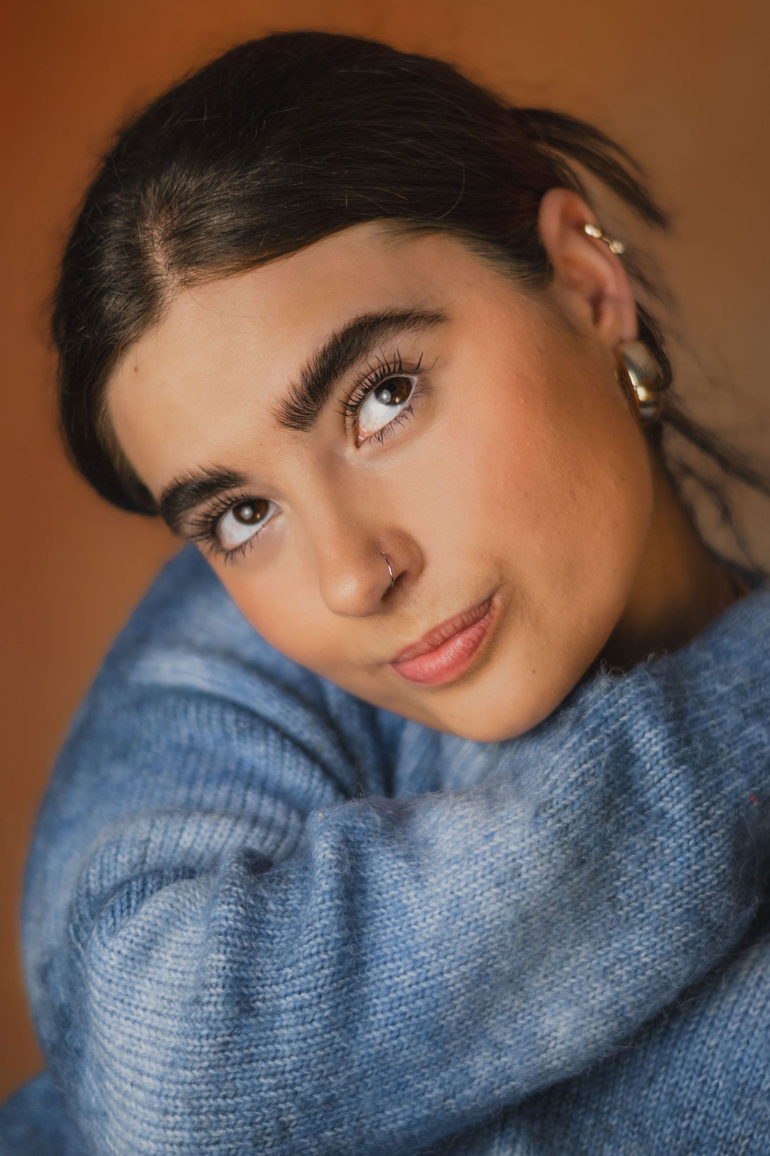 Portrait series showing expressive close-ups wearing cozy blue sweater against warm brown background.