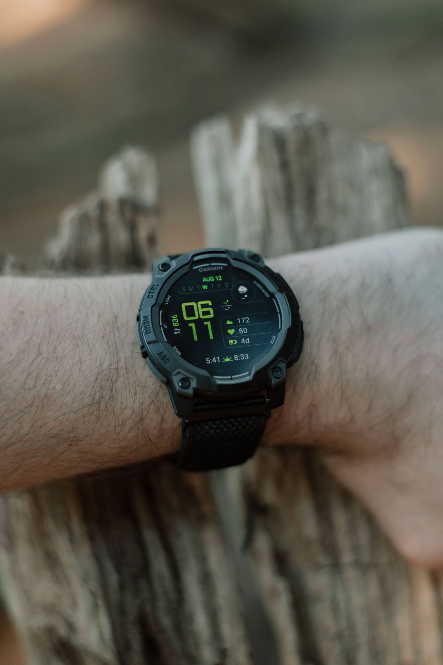 Black tactical smartwatch with green digital display on a man's wrist against rustic wood background.