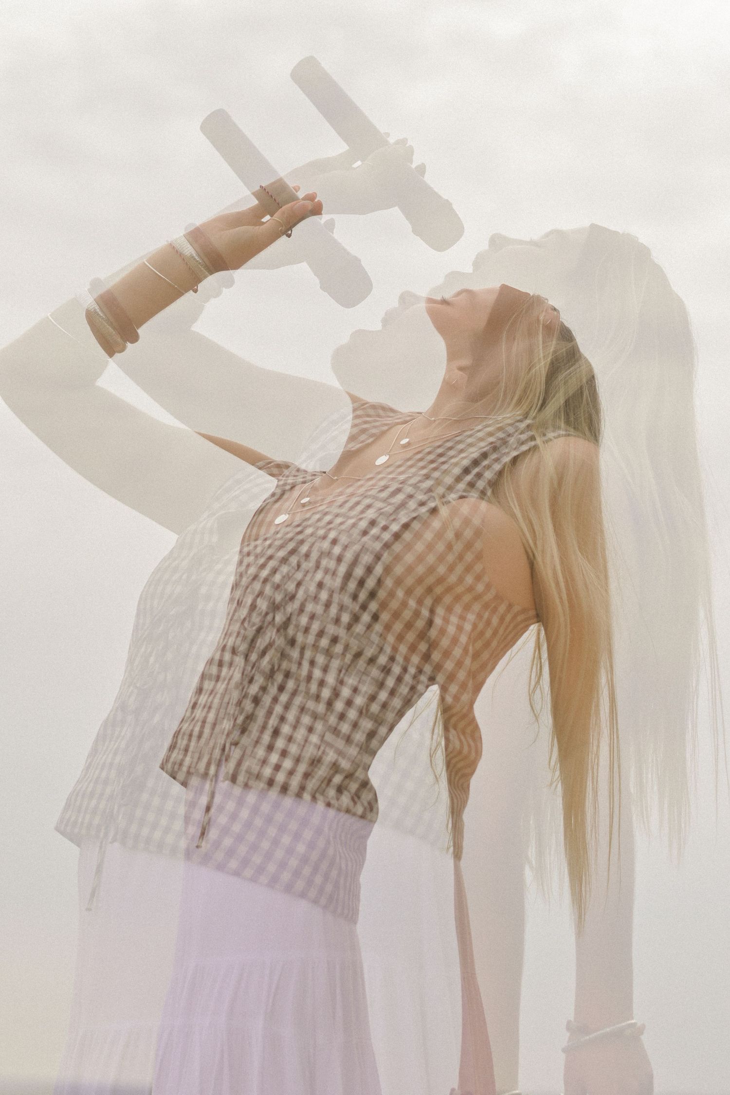 Double exposure of person dancing in white dress and gingham top against bright background.