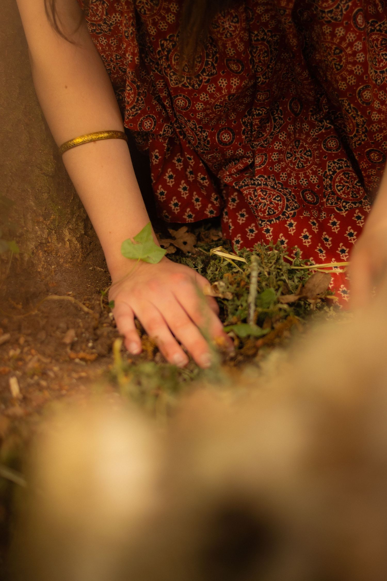 Close-up detail of hands gently touching ground while wearing a patterned burgundy dress.