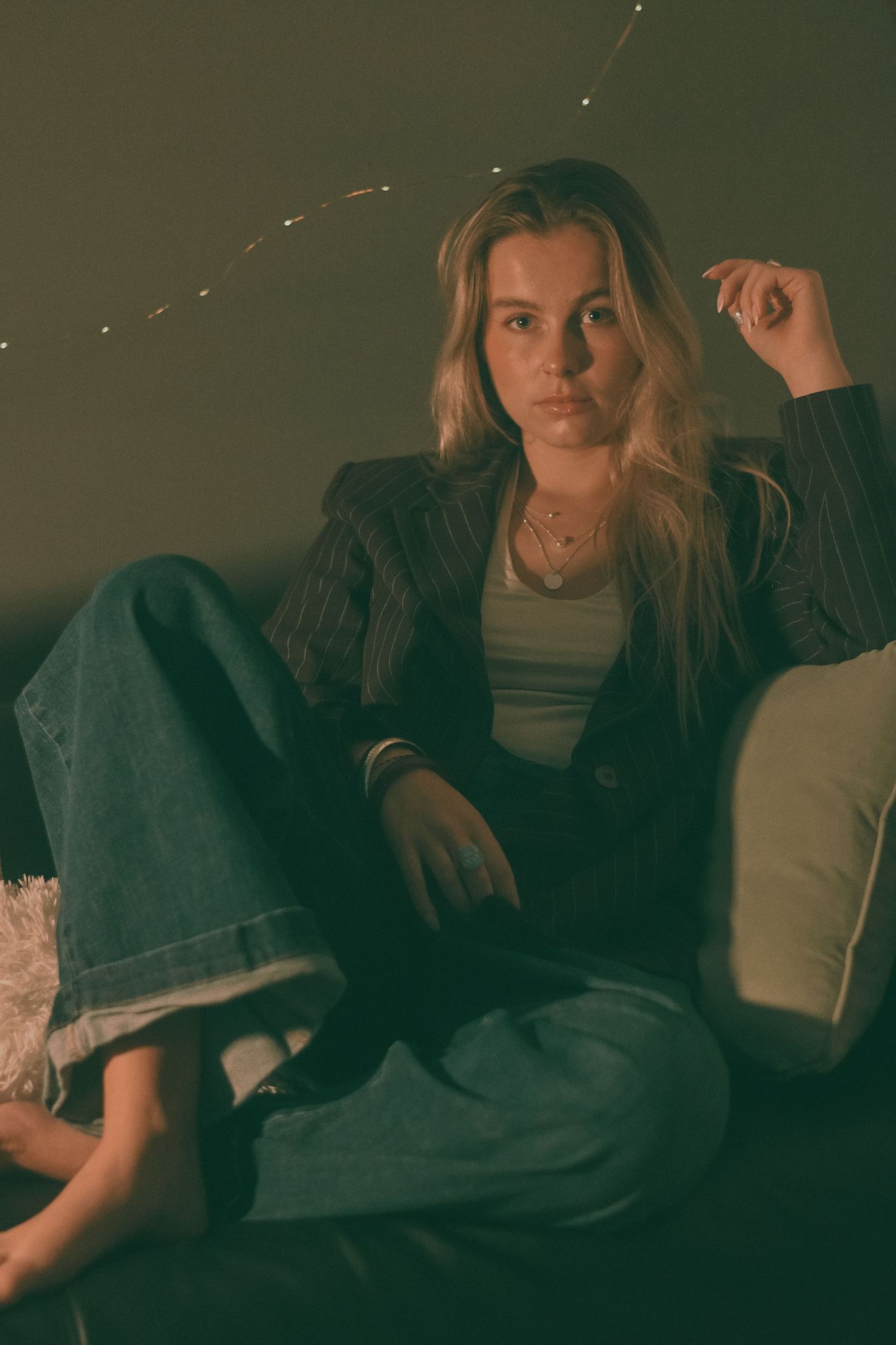 Casual portrait on couch wearing denim and black jacket in moody lighting.