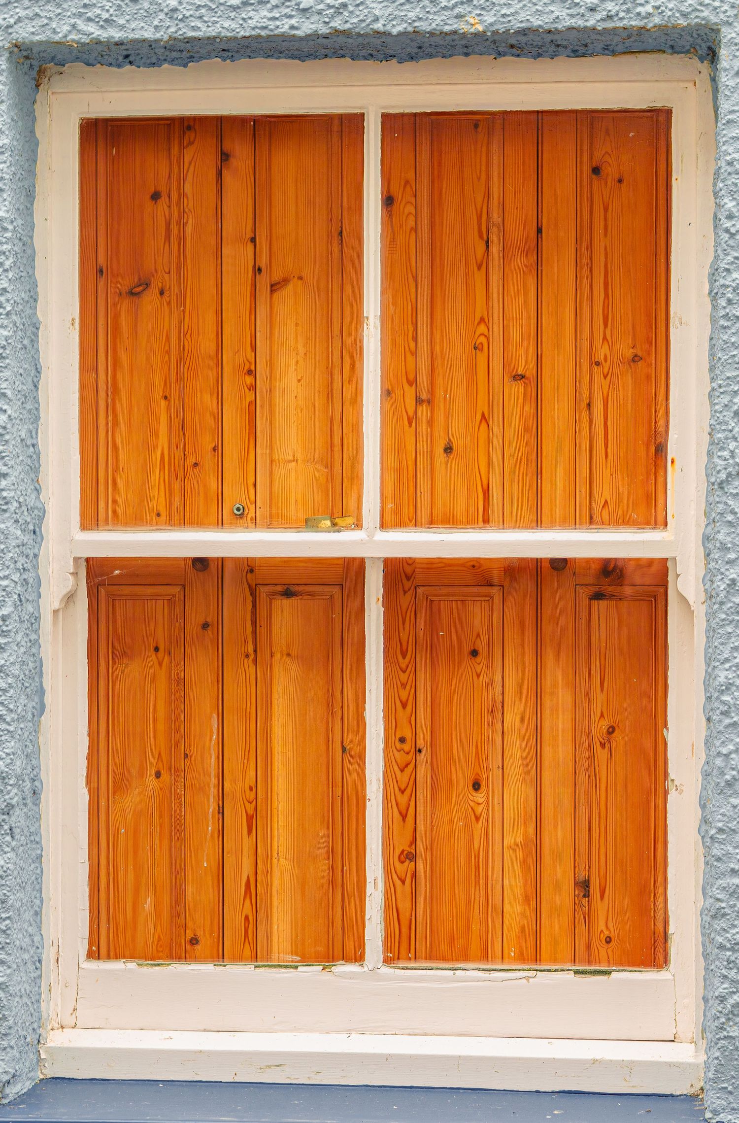 White window frame with natural pine wooden panels on textured grey wall.