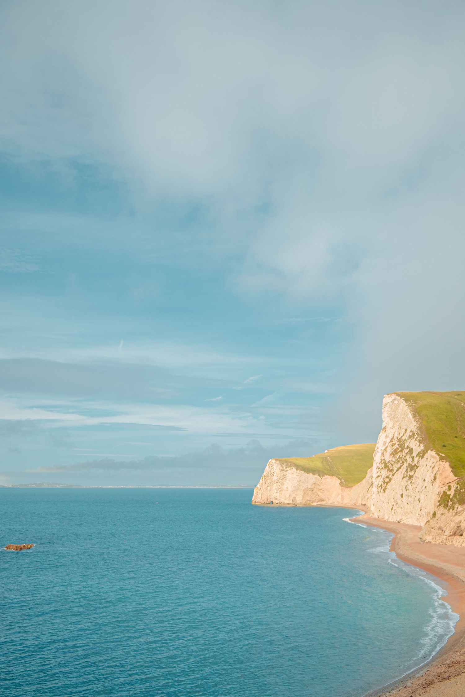 Dramatic coastal landscape with white cliffs and turquoise ocean under blue sky.