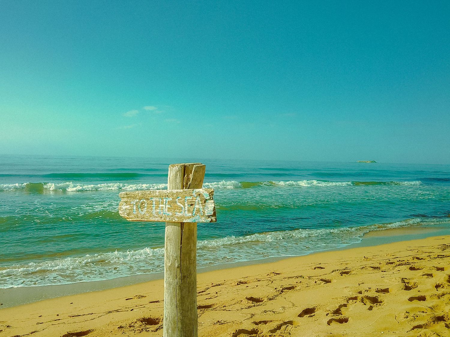 Wooden post on sandy beach with turquoise ocean waves rolling in.