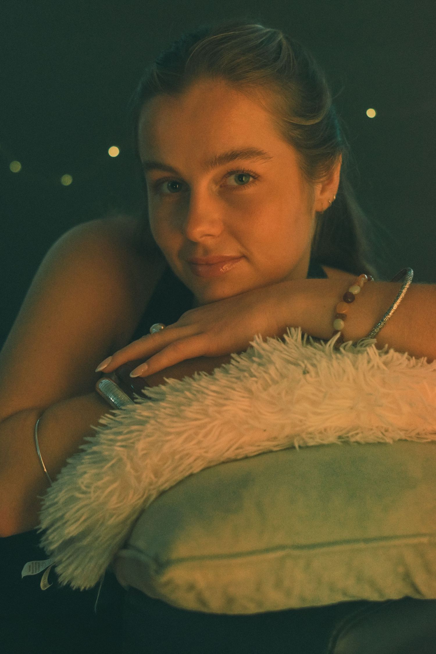 Atmospheric evening portrait with plush cushion and twinkling lights.