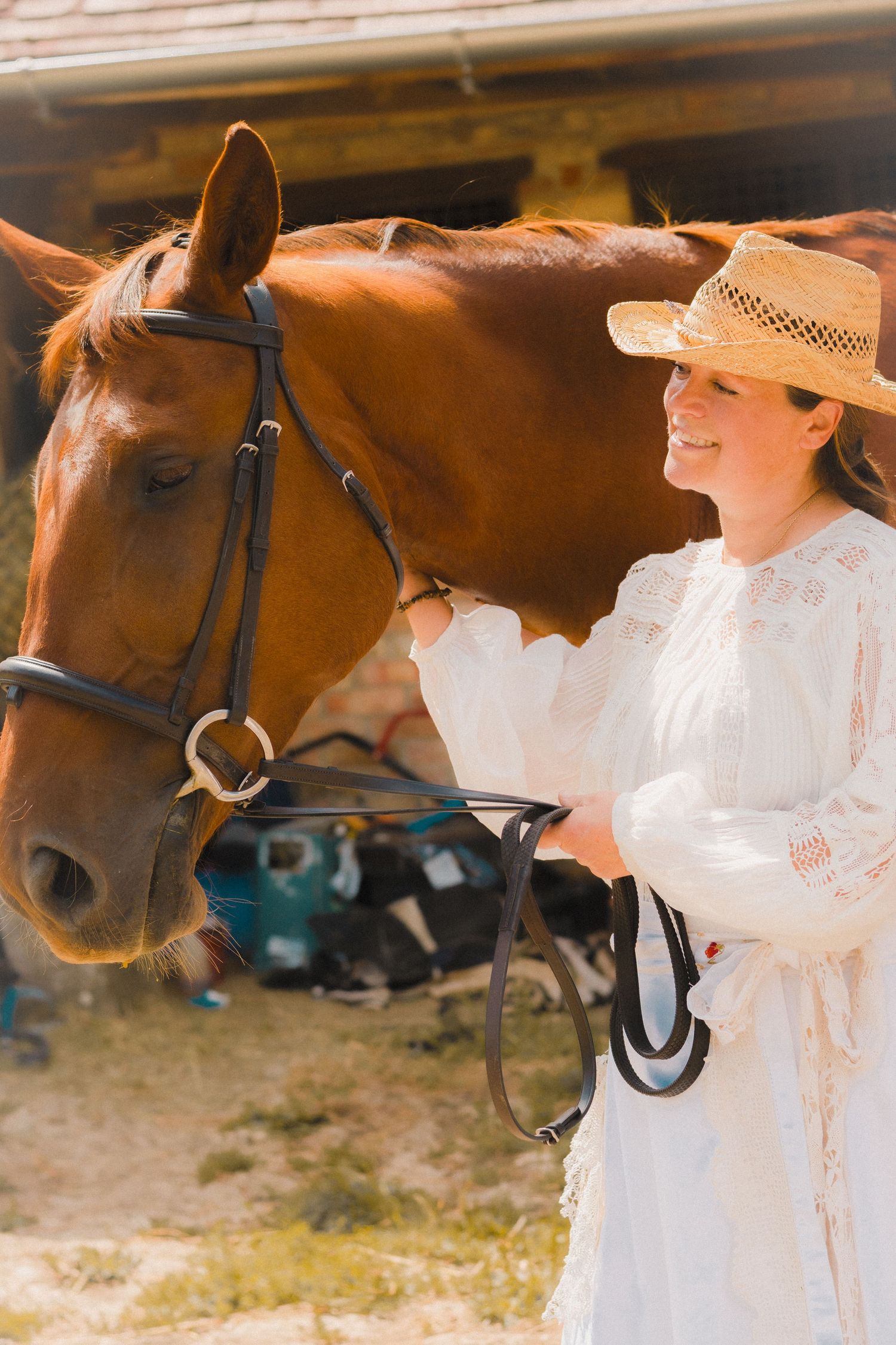 A gentle interaction between a chestnut horse and someone in a white lace dress wearing a straw hat.