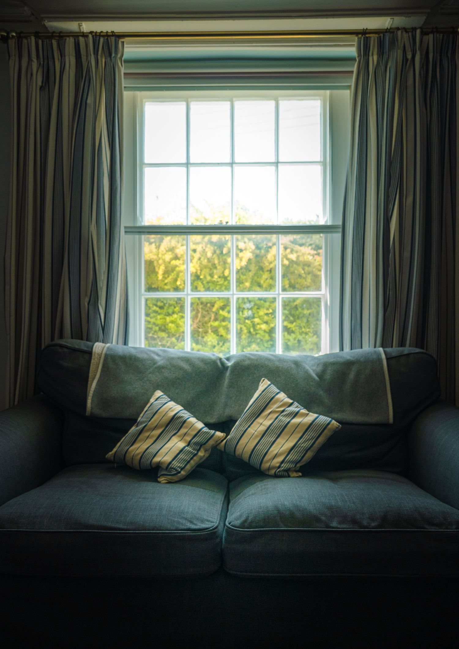 Dark grey couch with striped pillows beneath a large window with curtains.