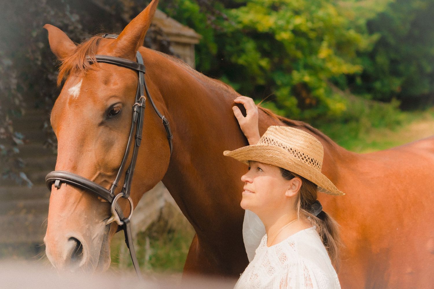 Close-up profile of a chestnut horse with someone in vintage attire against natural scenery.