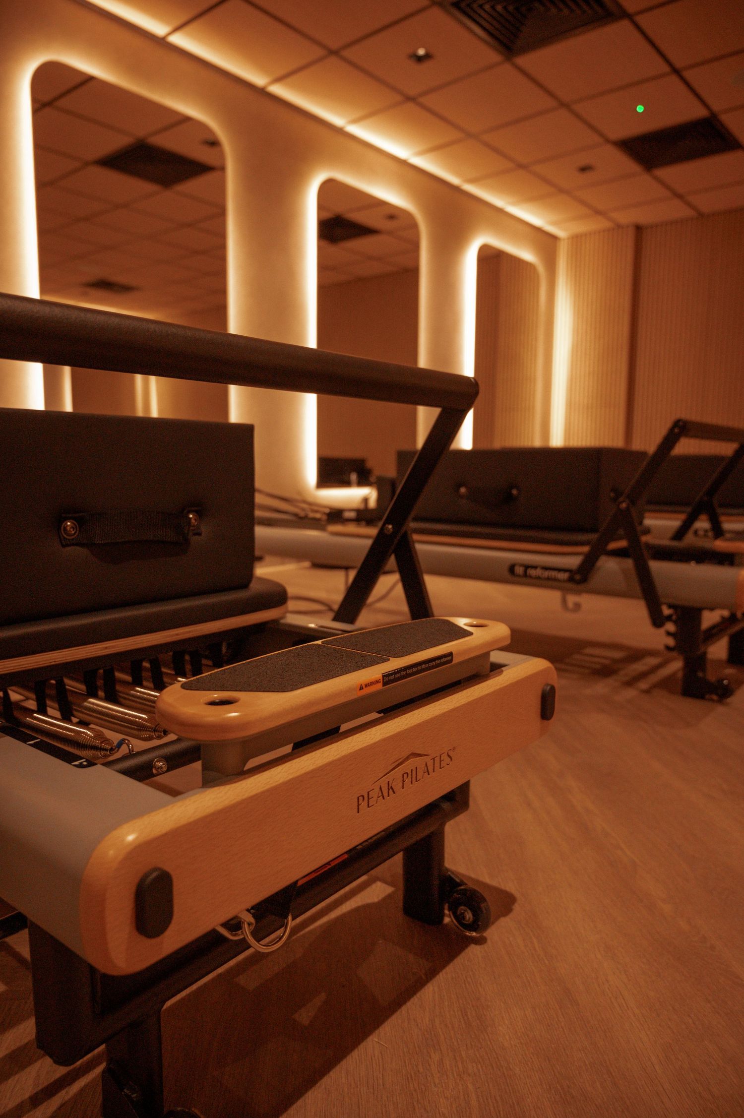 Peak Pilates reformer machines in a warmly lit studio with illuminated arch mirrors reflecting elegant equipment rows.