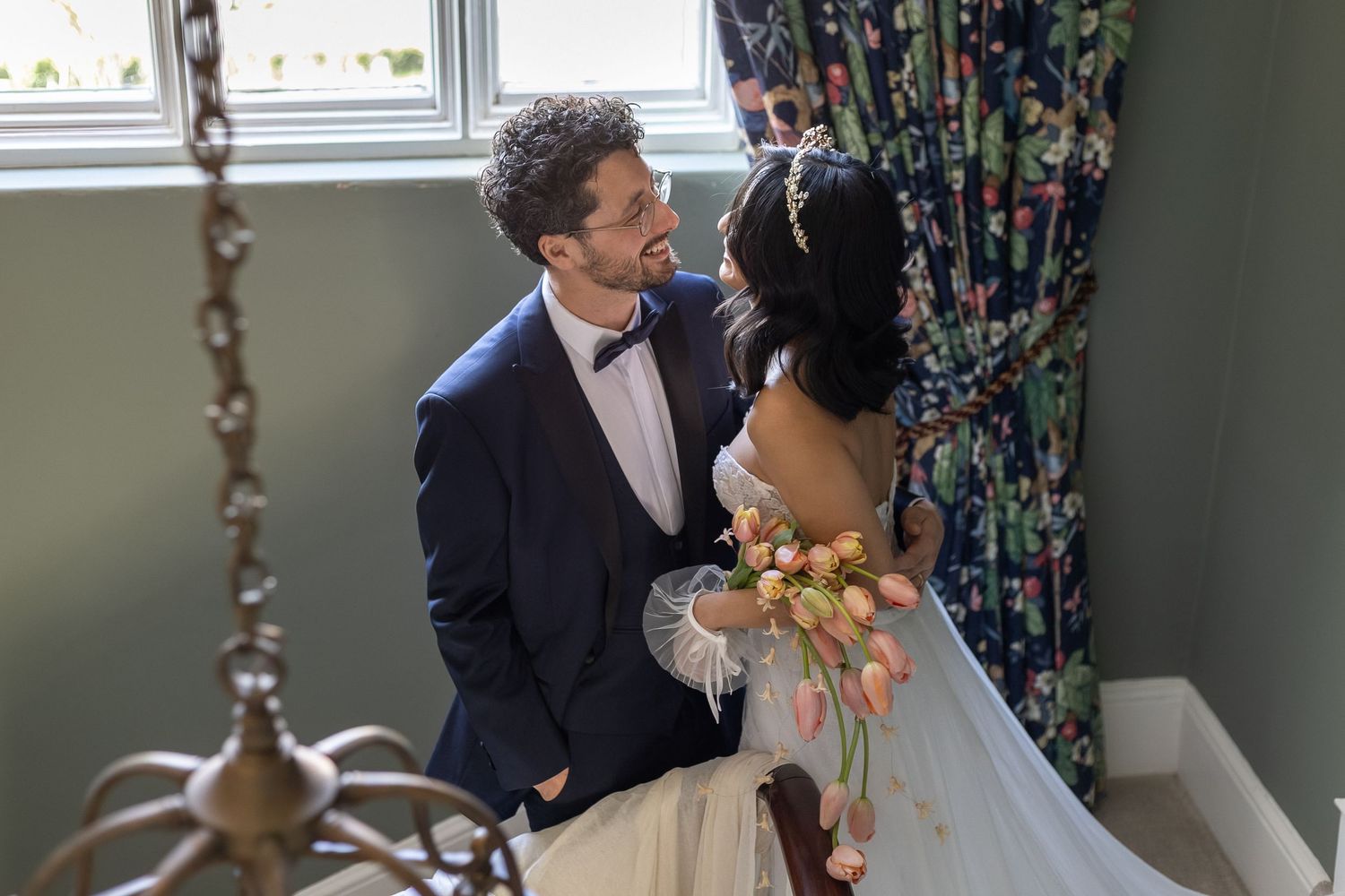 A couple shares a romantic moment during their wedding ceremony in a sunlit room with floral decorations.