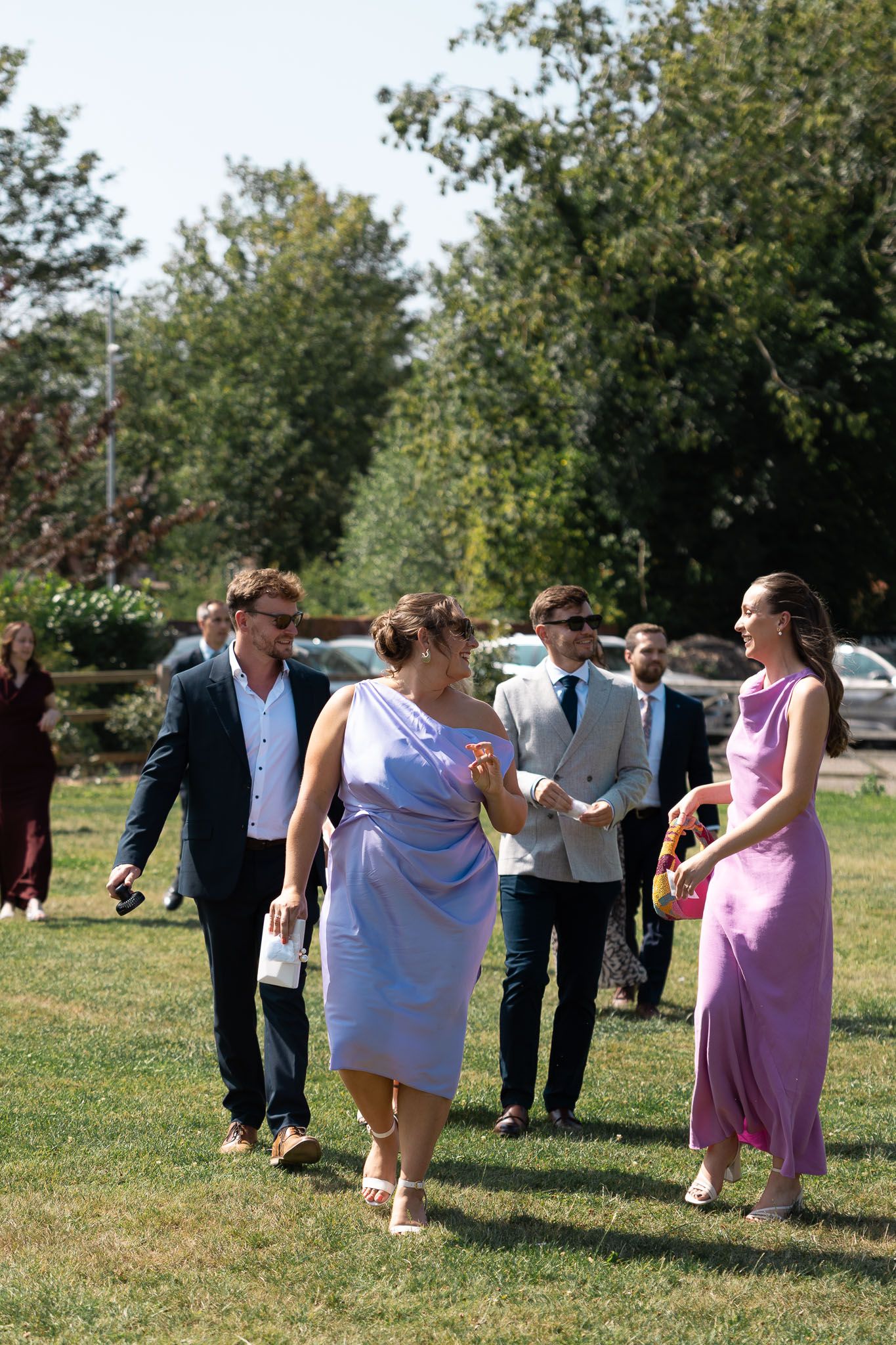 Wedding guests mingle on a sunny lawn during outdoor reception festivities.