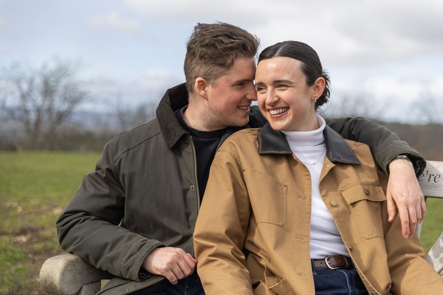 Two people share a candid moment together while sitting outdoors in casual winter clothing.