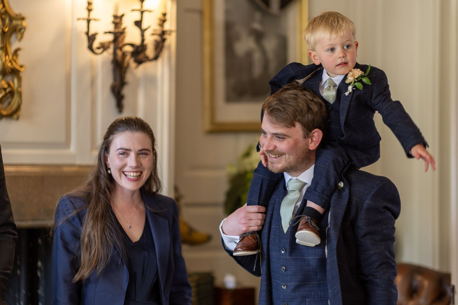 Joyful wedding party interactions in formal attire against classic interior backdrop.