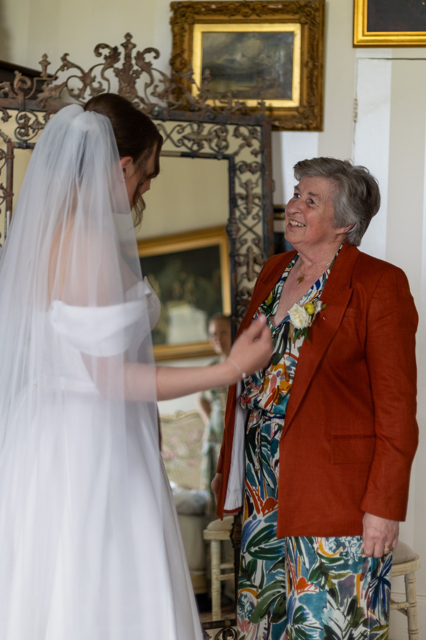 Candid moments of wedding preparation in a room decorated with vintage paintings and ornate frames.