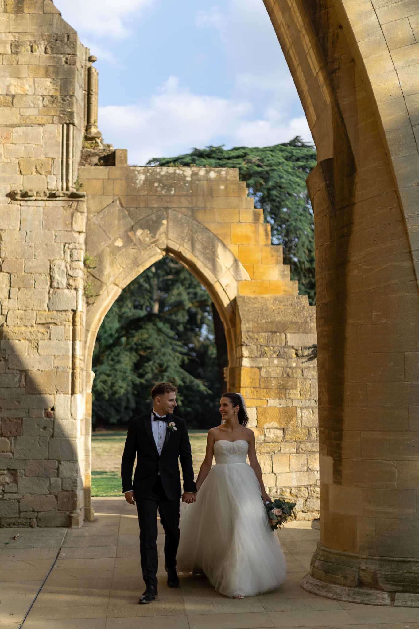 Couple walks through historic stone archways during wedding photoshoot.