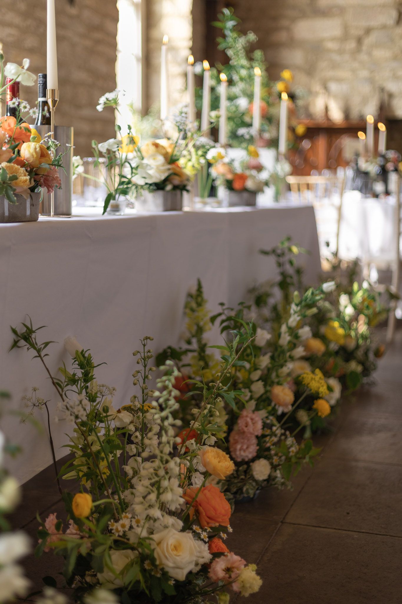 Elegant floral table arrangements with peach and white flowers line a rustic stone venue.