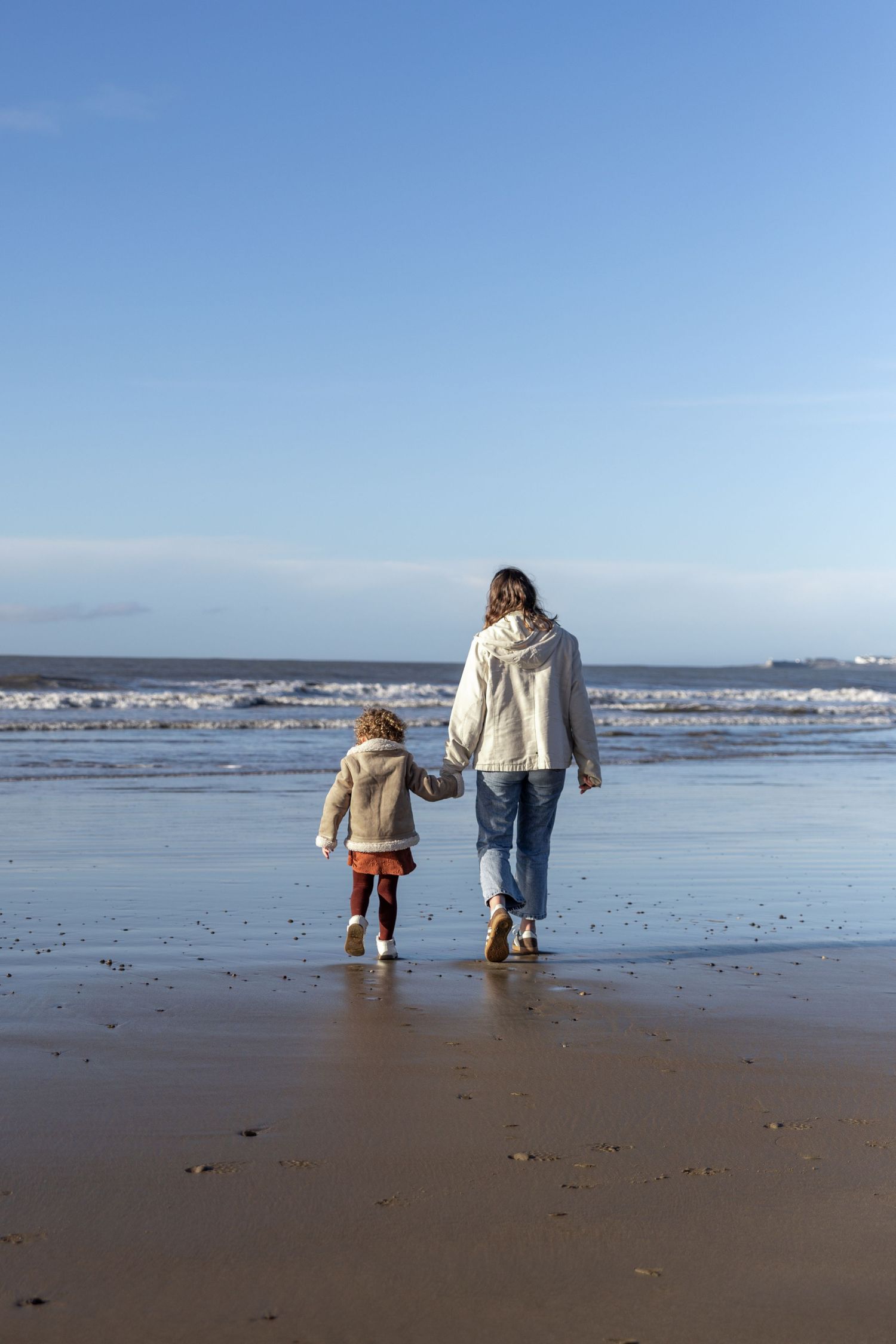People walking and exploring together on a sandy beach with gentle waves and seabirds on a clear sunny day.