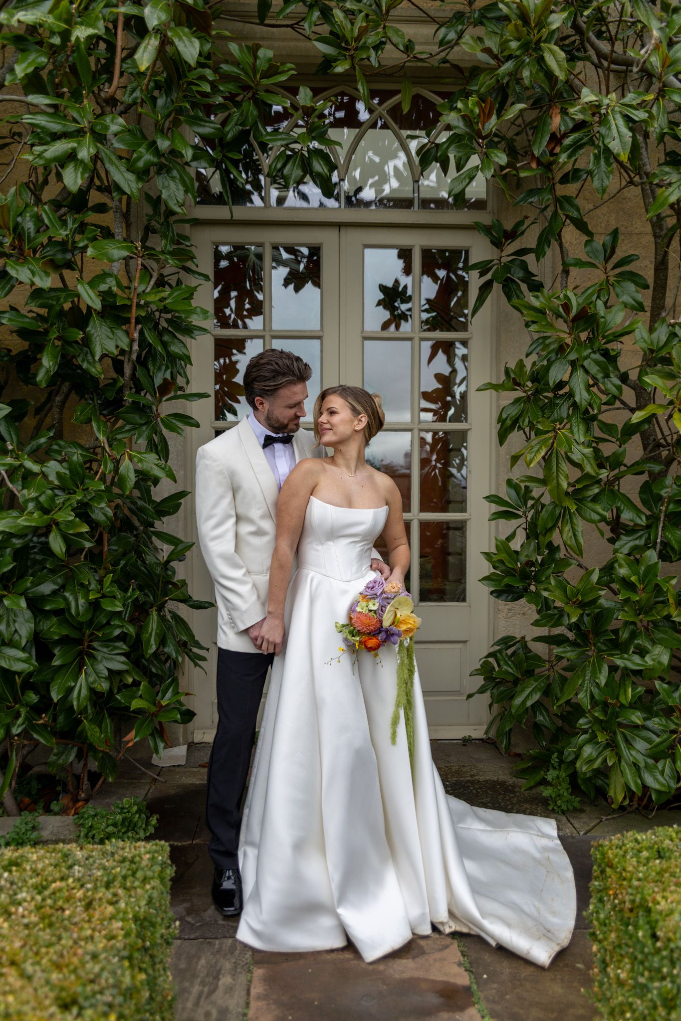 A wedding couple shares an intimate moment in front of a lush garden backdrop.