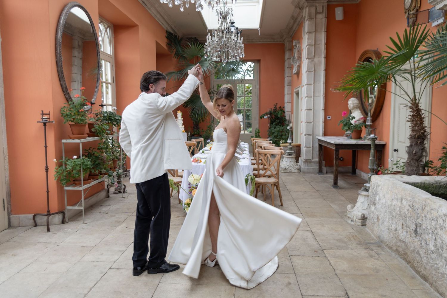 Newlyweds dancing together in an elegant coral-colored courtyard with crystal chandeliers.