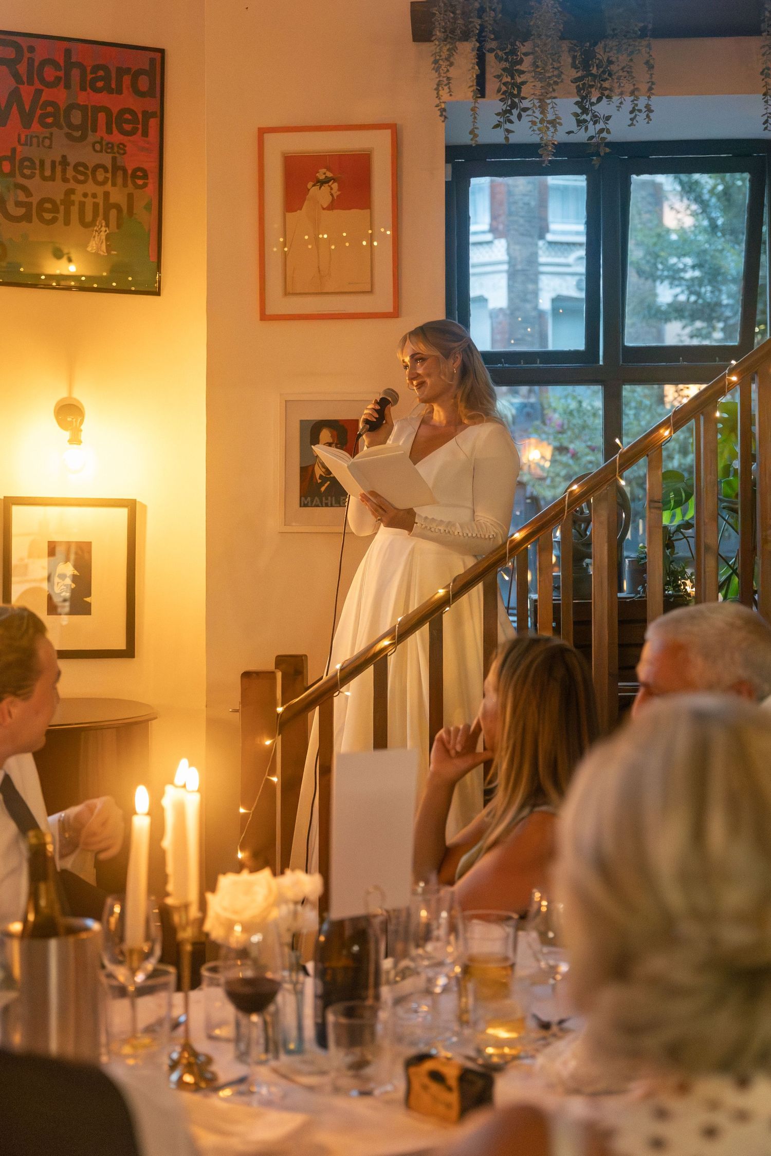 Bride in white gown gives speech at candlelit wedding reception dinner at the Fidelio Cafe, London