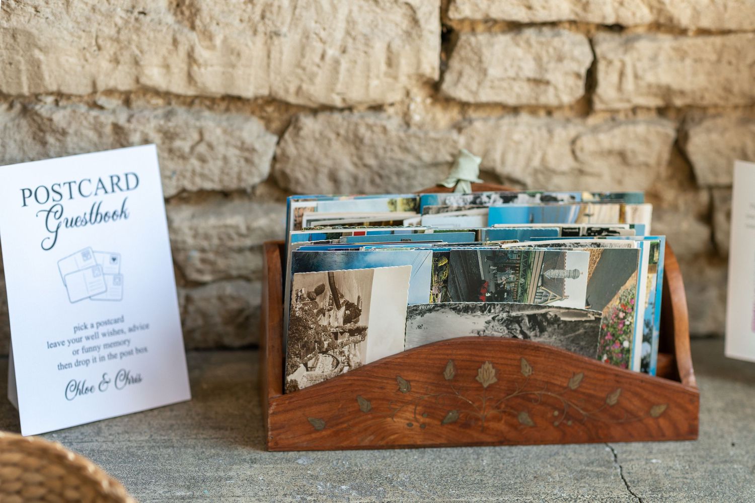 Wooden postcard guestbook holder filled with colorful postcards displayed on a stone ledge at a wedding reception.