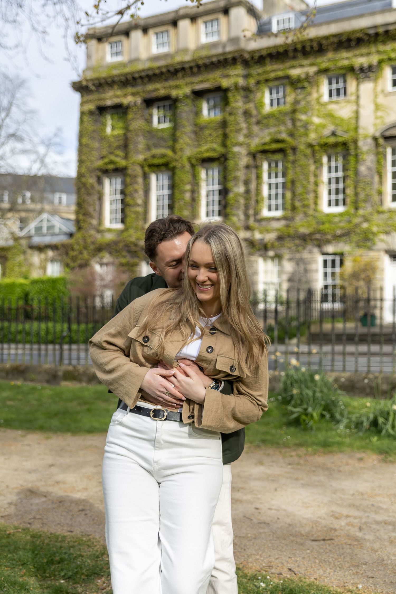 Happy couple embracing outdoors in front of an ivy-covered historic building in spring.