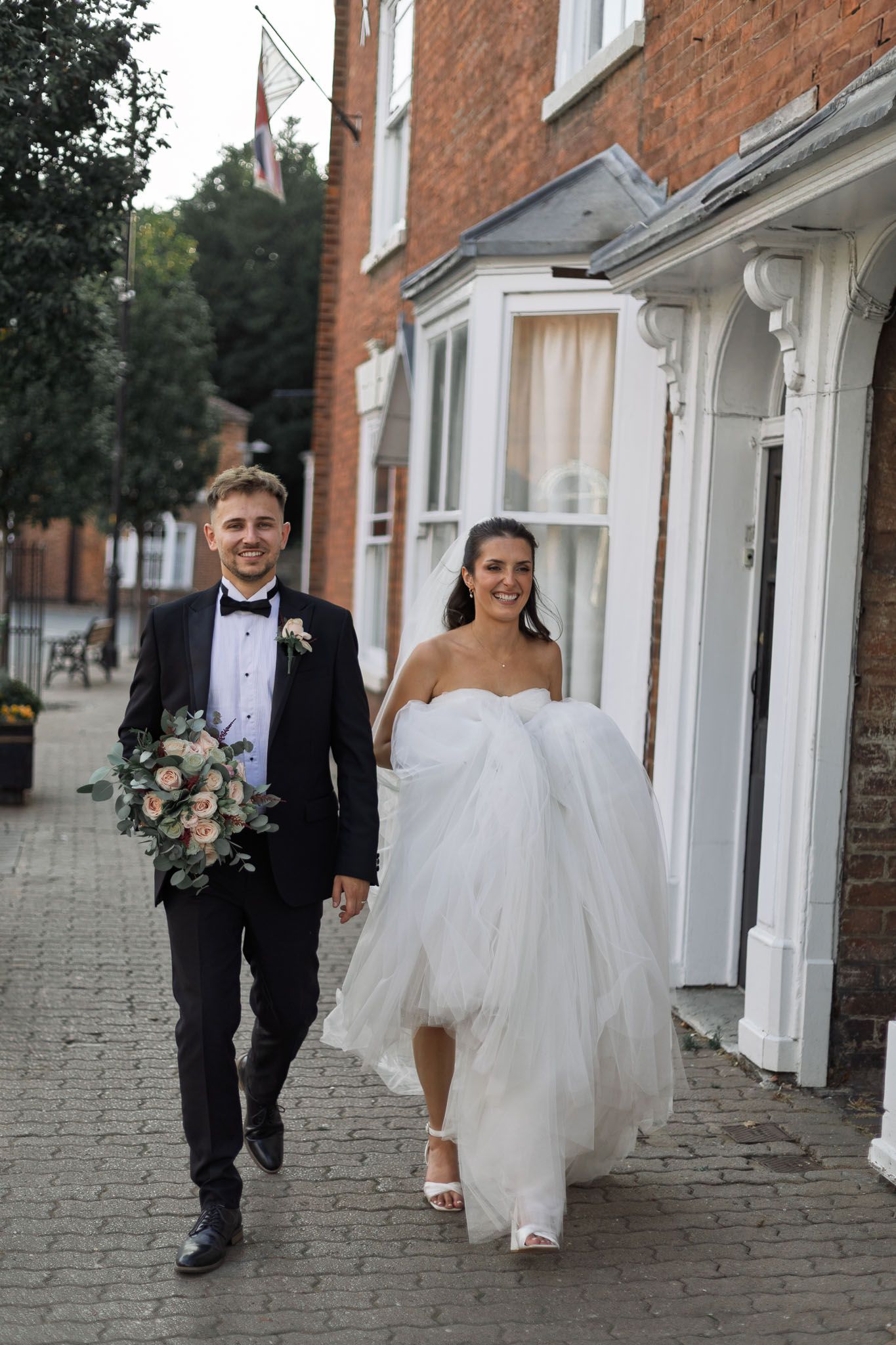 Newlyweds walk along brick building sidewalk after ceremony.