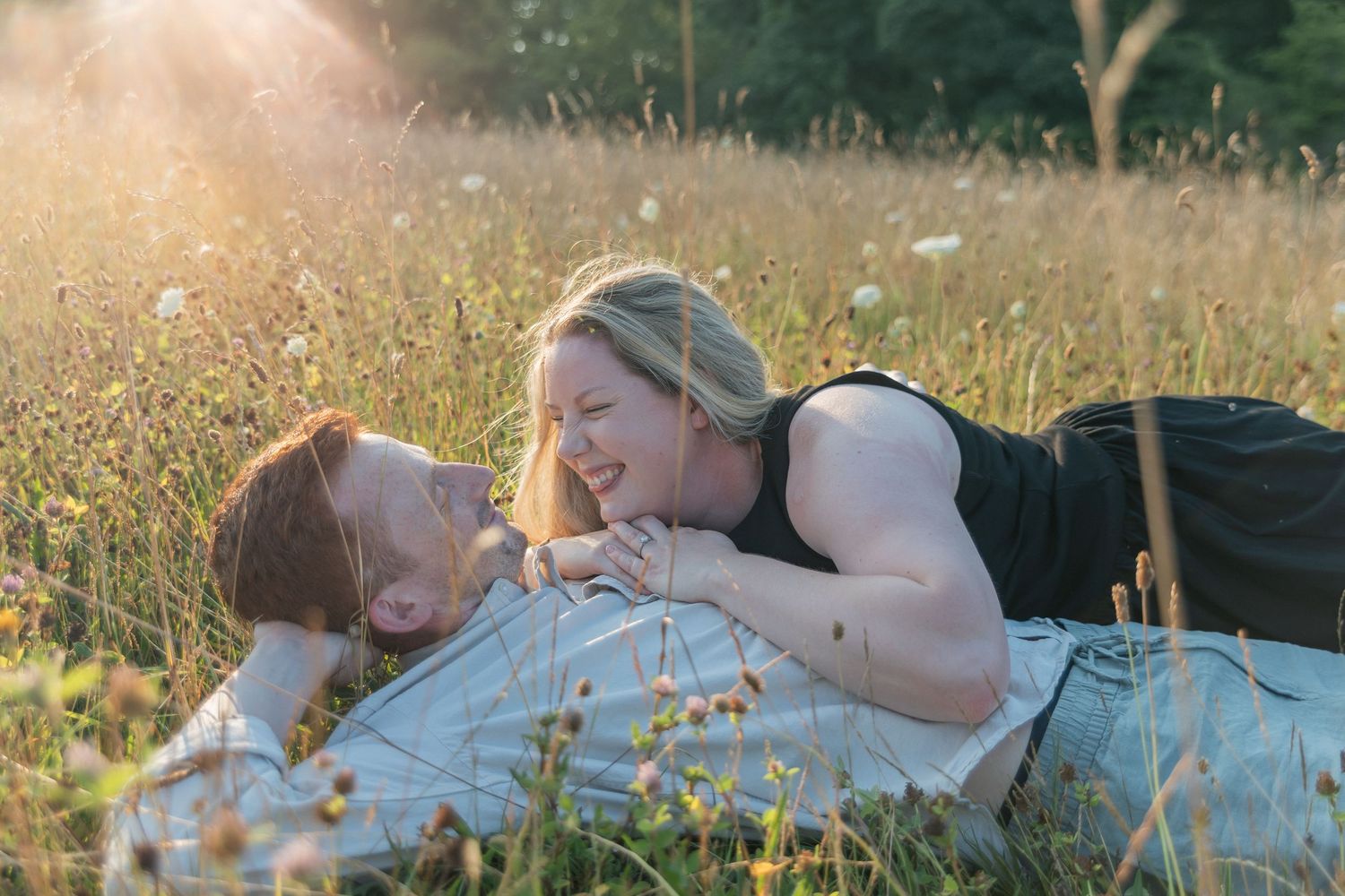 Couple laughing and lying together in a sunny wildflower meadow during golden hour.
