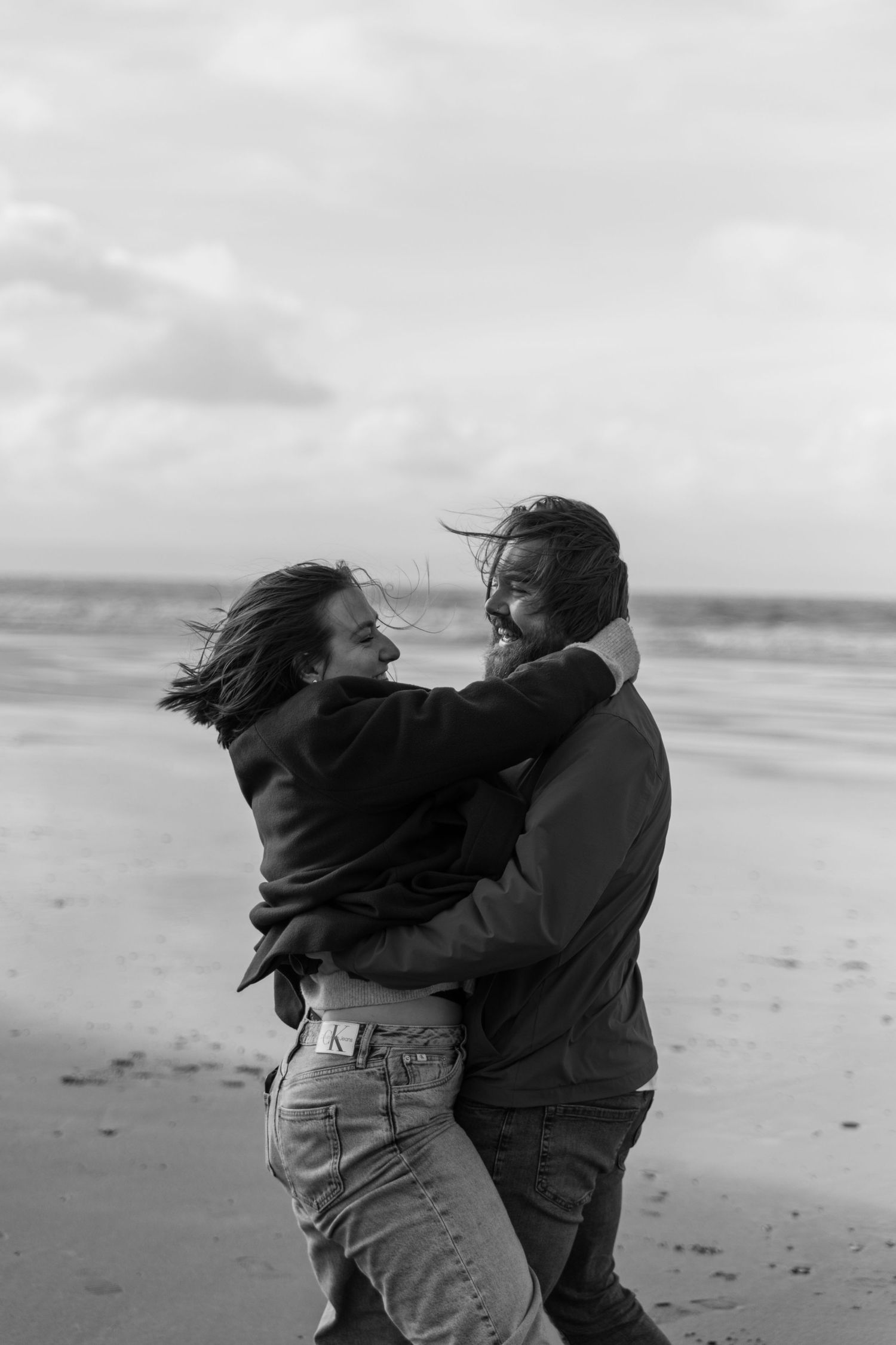 Relaxed documentary images by a Wiltshire wedding photographer. Black and white photo of two people dancing together on a windswept beach.