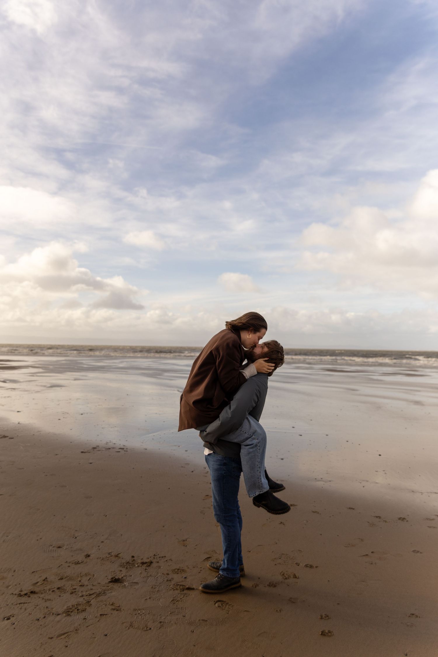 A couple shares a romantic moment on an overcast beach, photographed by a documentary wedding photographer in Wiltshire