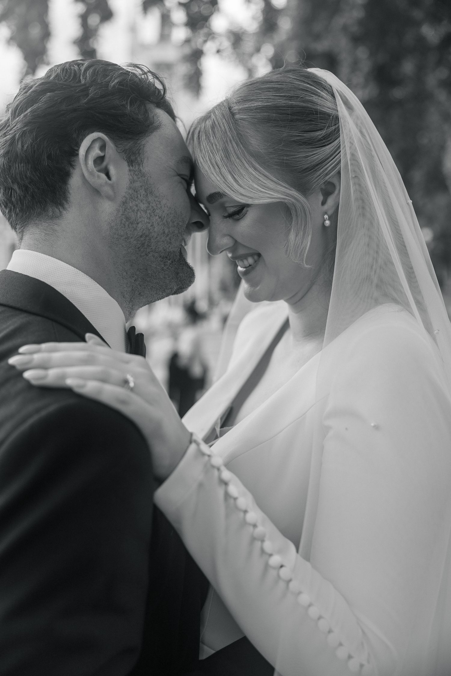 Black and white photo of a smiling bride in veil and groom in tuxedo sharing an intimate moment in London.