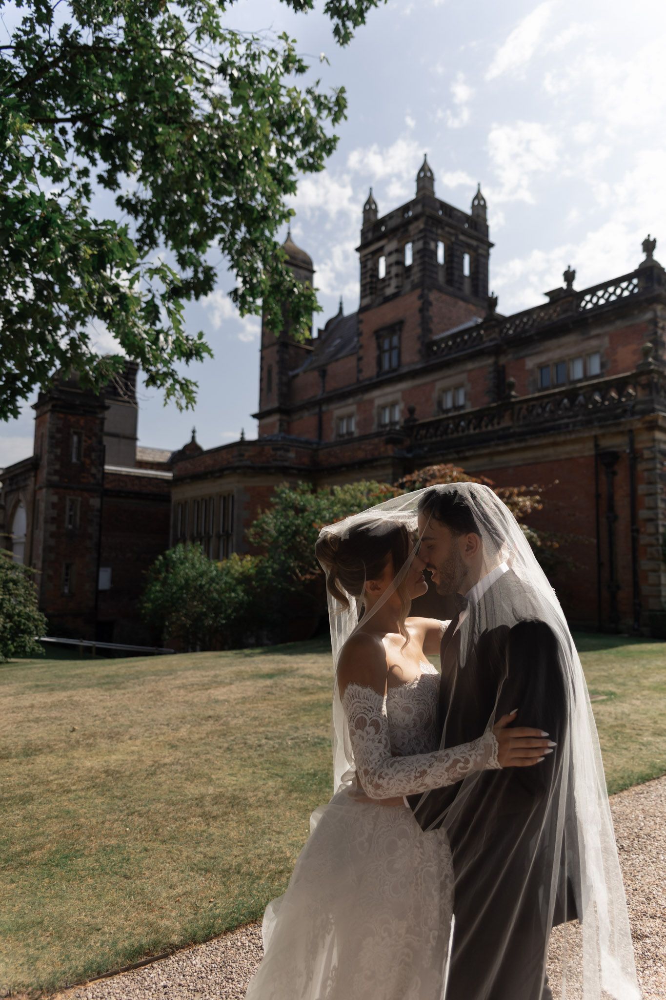 Newlyweds embrace in front of a grand Gothic-style brick building with ornate architecture.