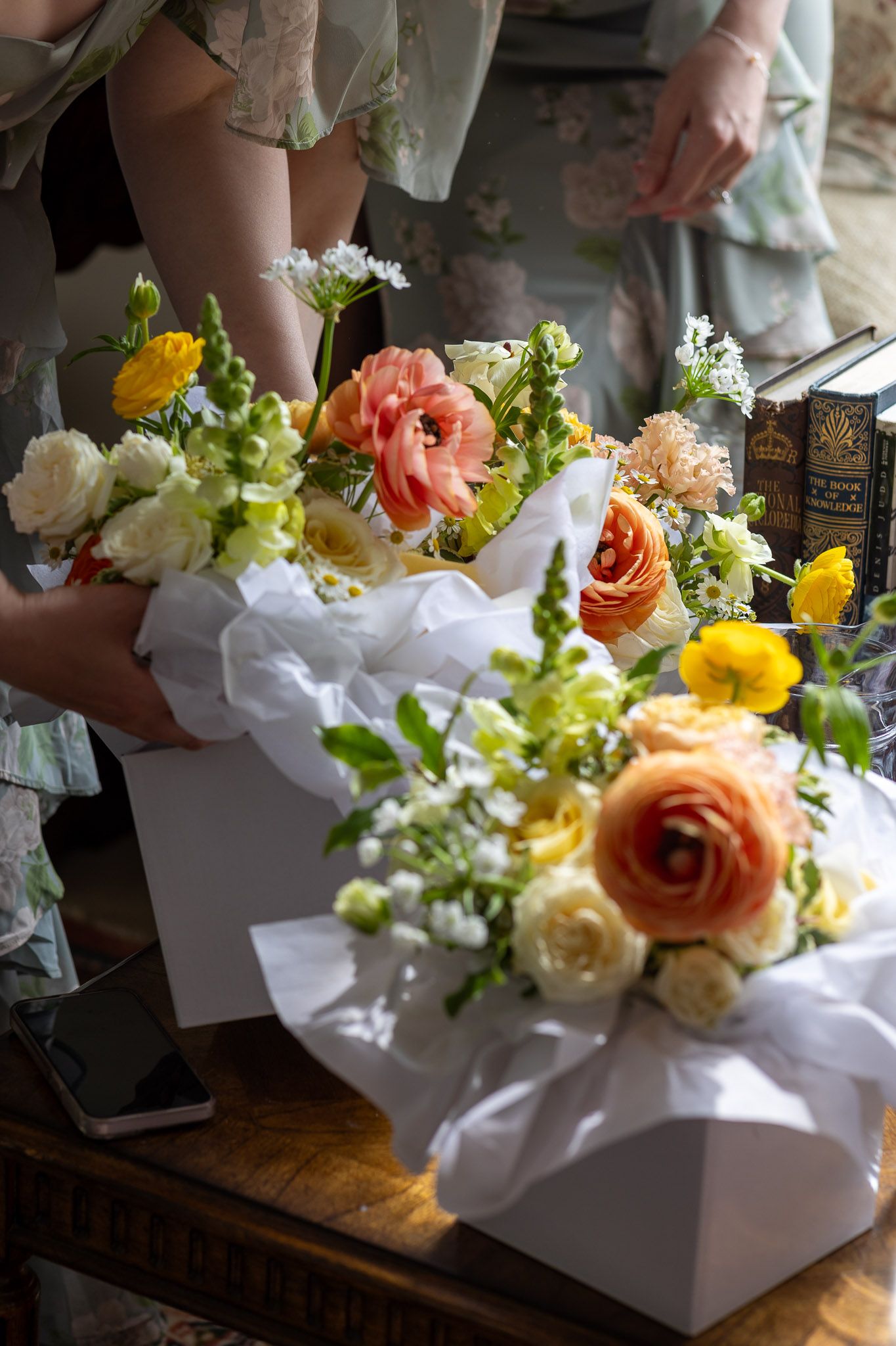 Three floral arrangements with roses and mixed flowers in white boxes sit on a wooden surface.