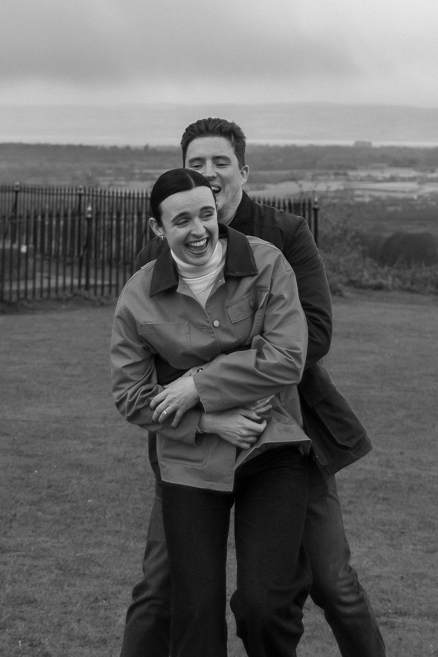 A playful black and white sequence showing two people embracing and laughing together in an outdoor field setting.