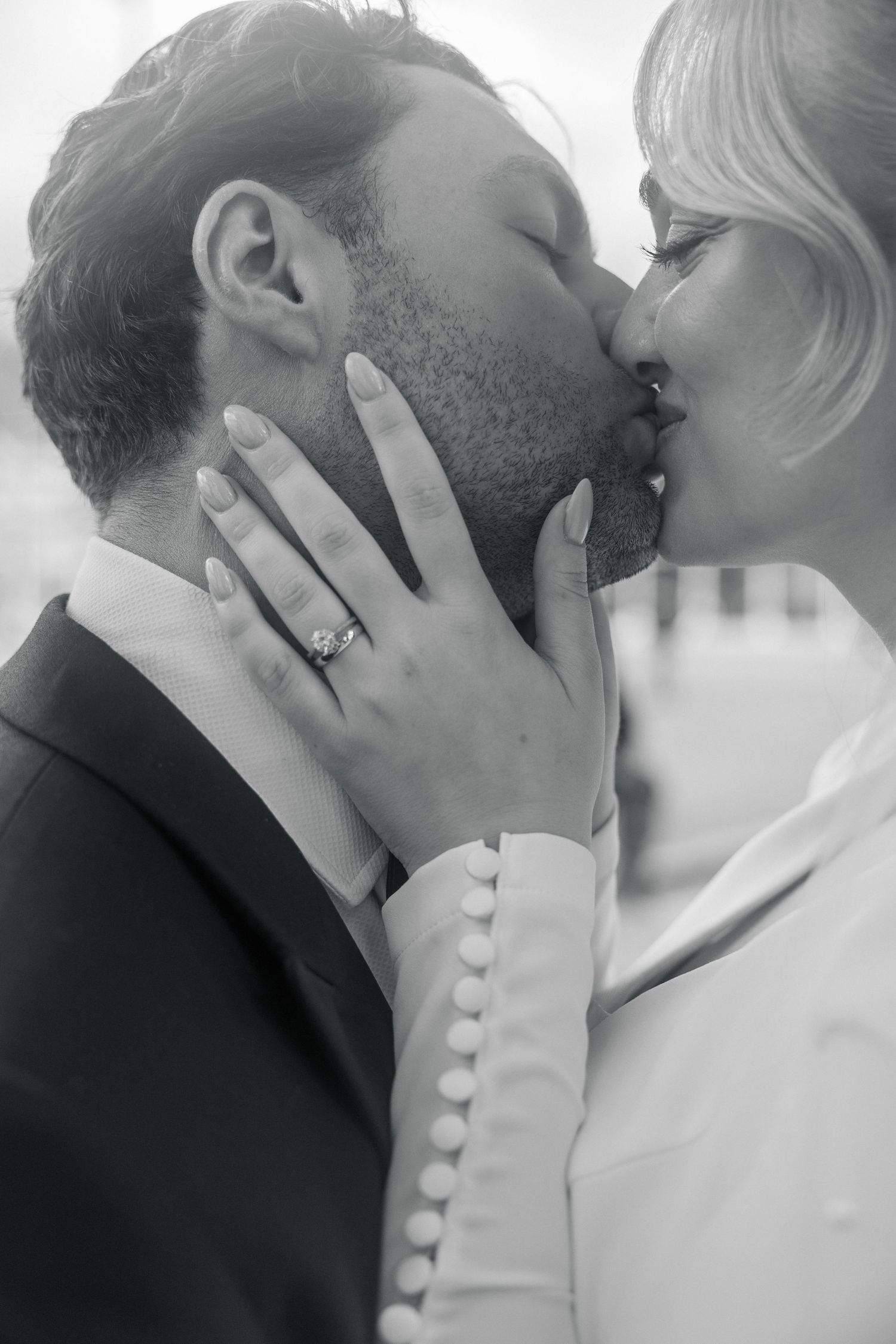 Black and white photo of a couple sharing a romantic kiss, bride wearing engagement ring and white gown in London