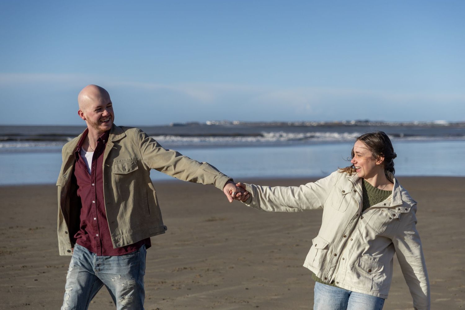 Two people walking together on a sandy beach during a cloudy day.