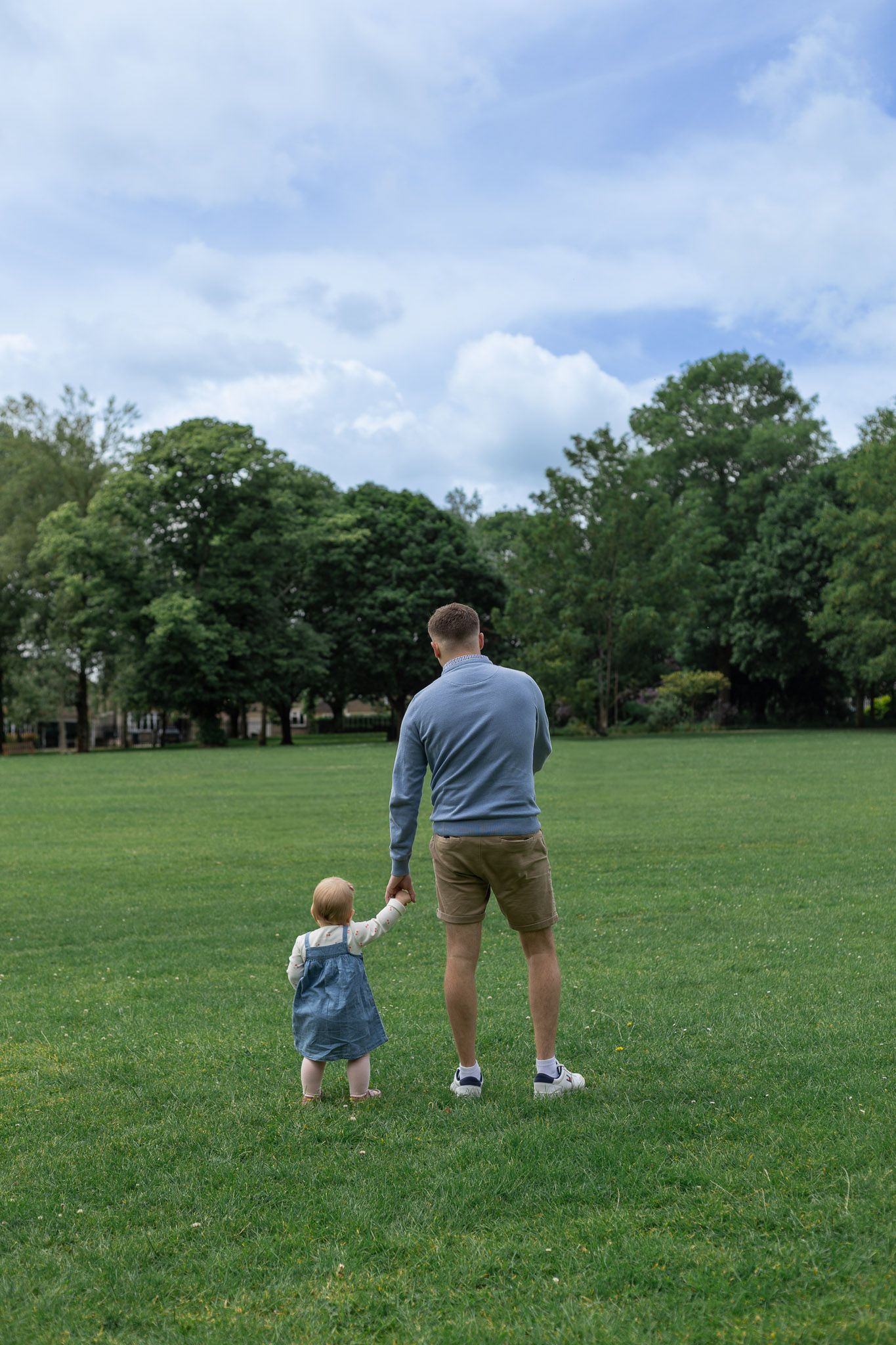 Two people walking together across a vast green field on a cloudy day.