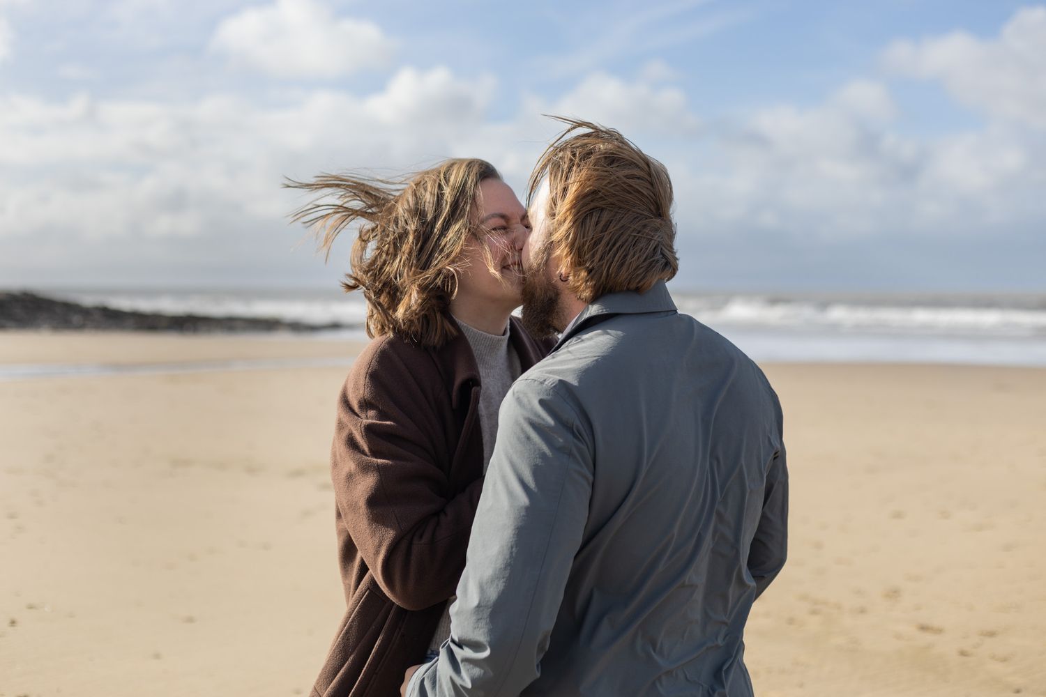 A tender moment captured on a sandy beach with ocean waves in the background.