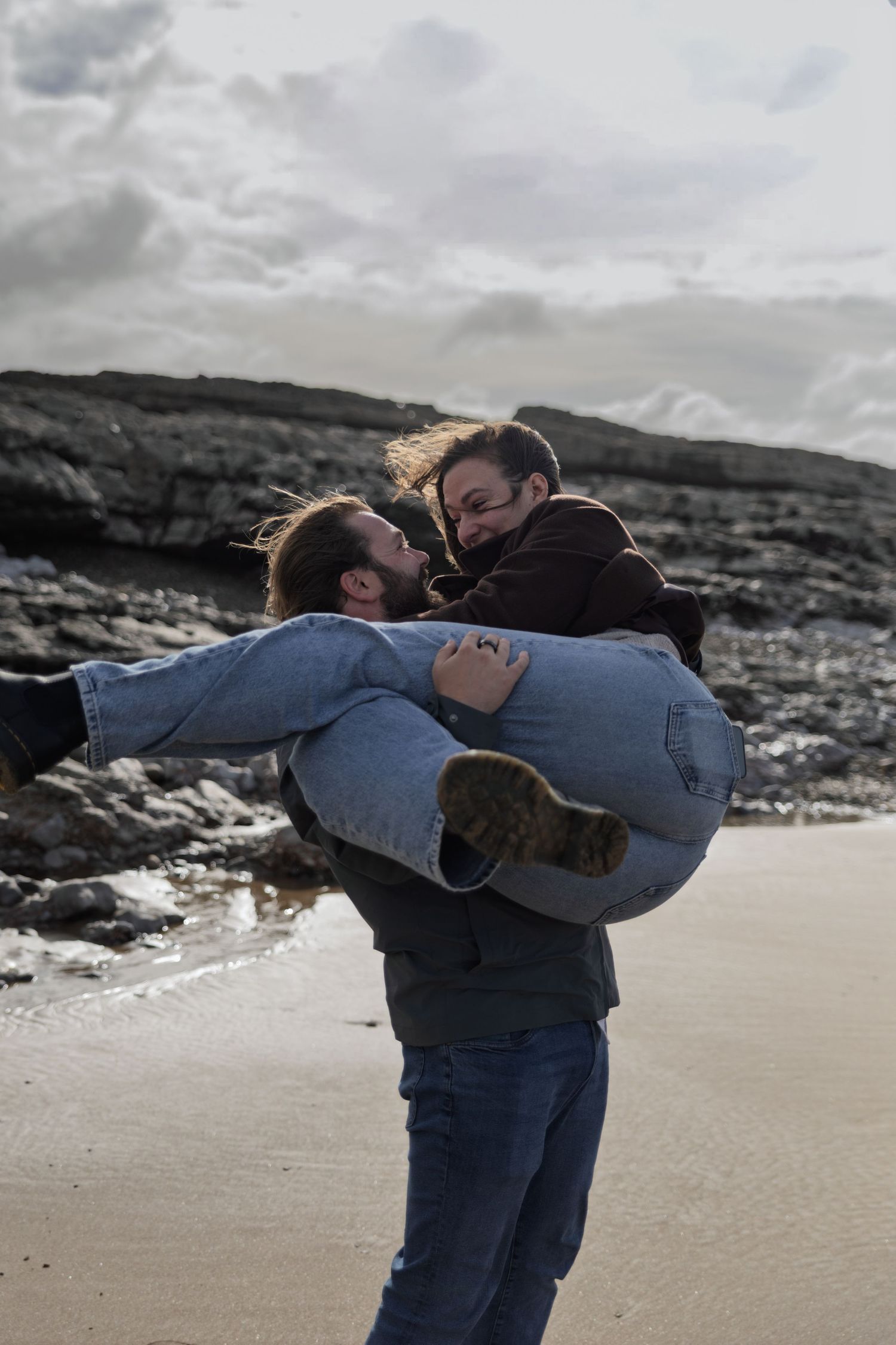 A couple embracing on a beach with a cloudy sky in the background.