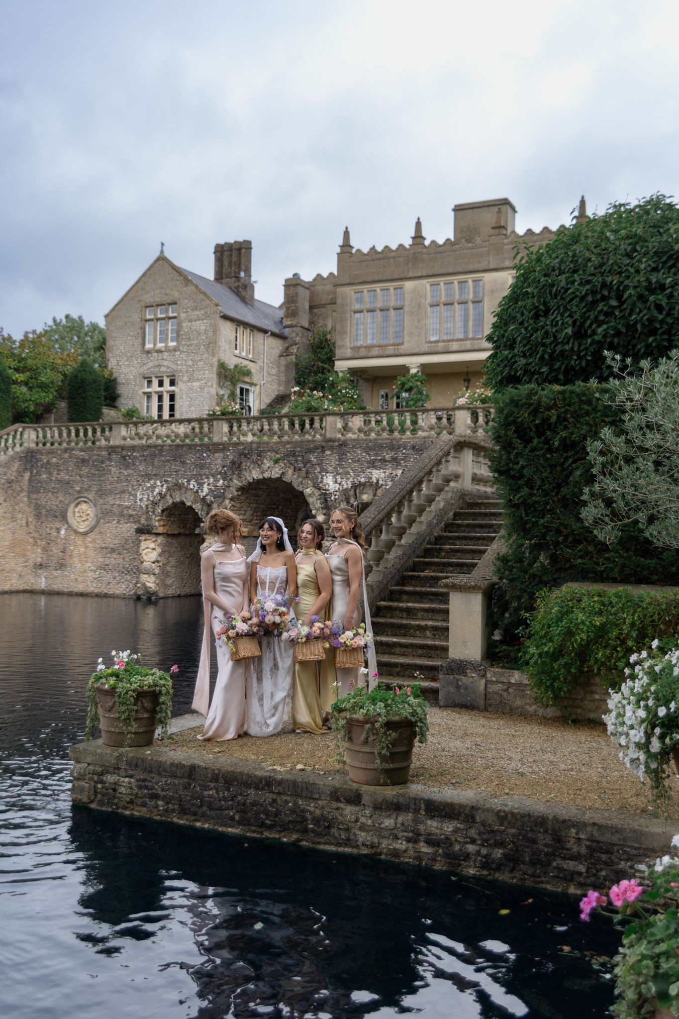 Wedding party poses on stone terrace overlooking dark water at historic estate.