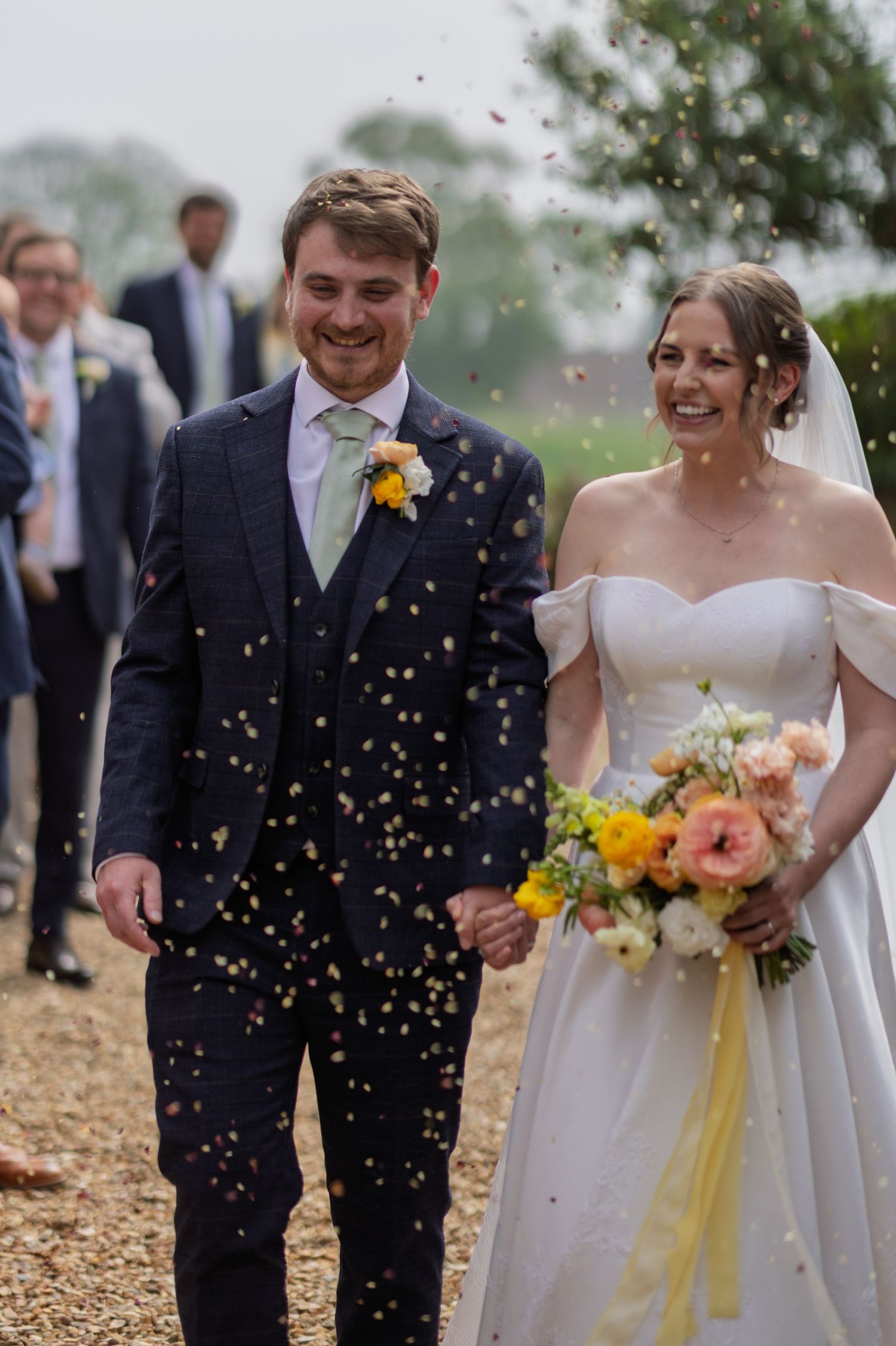 Wedding party walking outdoors while confetti falls around them in joyful celebration.
