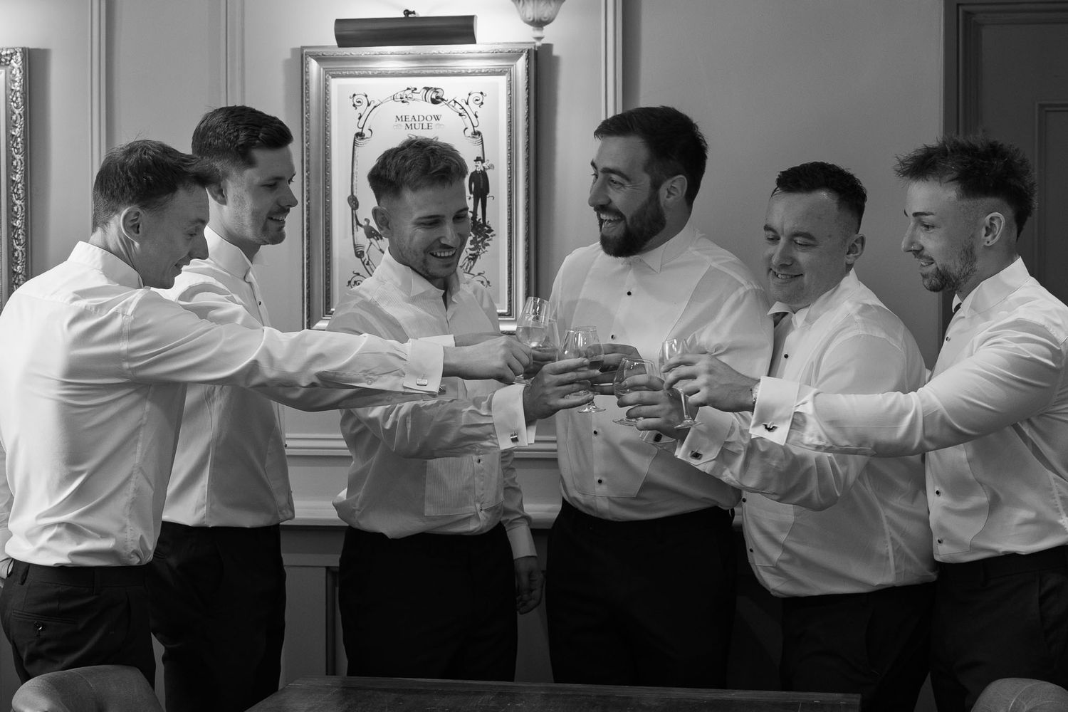 Groomsmen in white dress shirts playfully interact during wedding preparations.