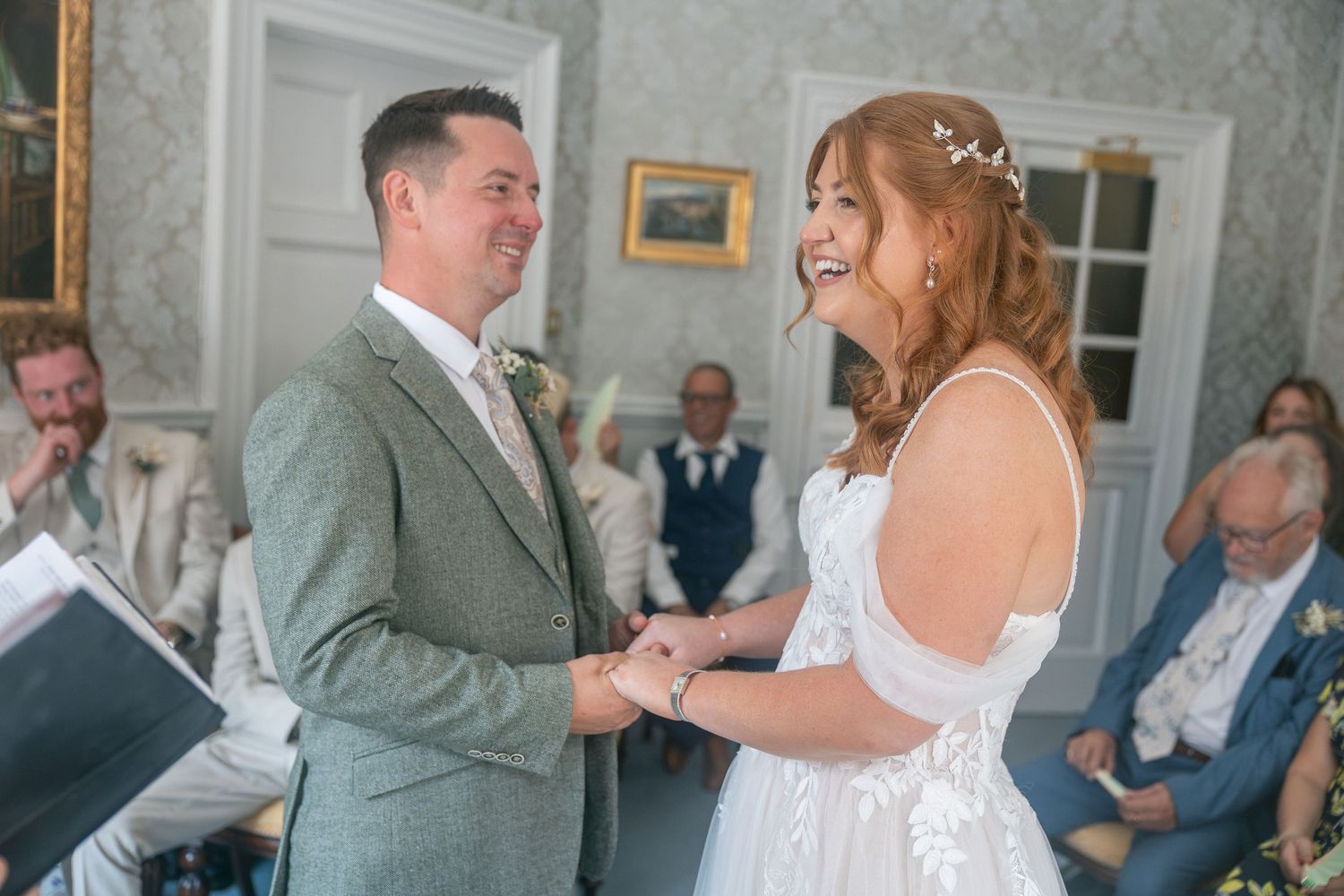 A joyful bride and groom exchange vows and hold hands during their elegant wedding ceremony at The Guildhall, Bath