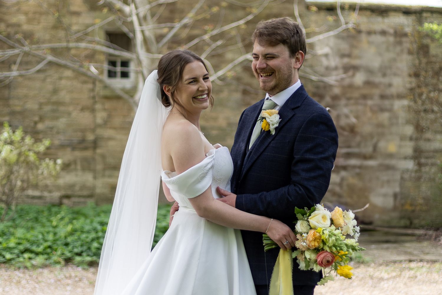 Newlyweds share a tender moment outdoors with the bride holding a vibrant yellow bouquet.